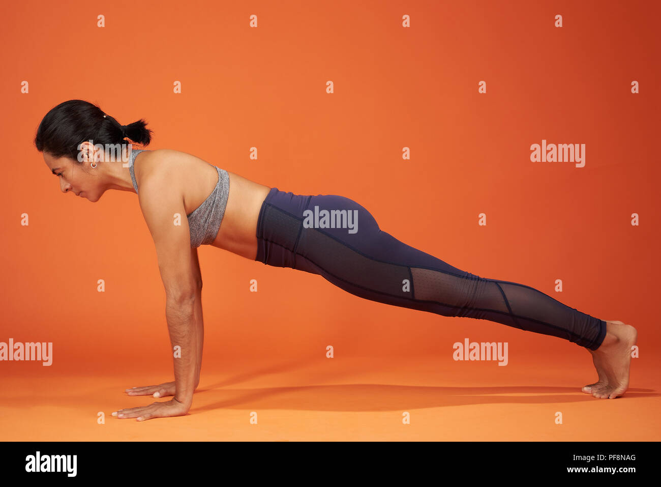 Plank yoga donna posa dimostrare su orange il colore di sfondo per studio Foto Stock