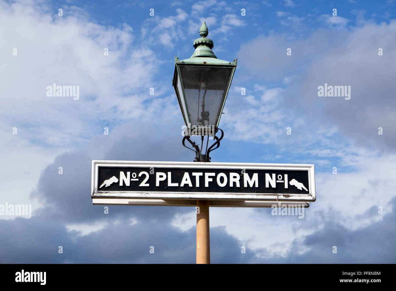 Vecchio segno di piattaforma con lampada in pullman alla stazione di patrimonio della linea ferroviaria. Presa dal basso angolo guardando in alto nel cielo blu e nuvole affascinante. Foto Stock