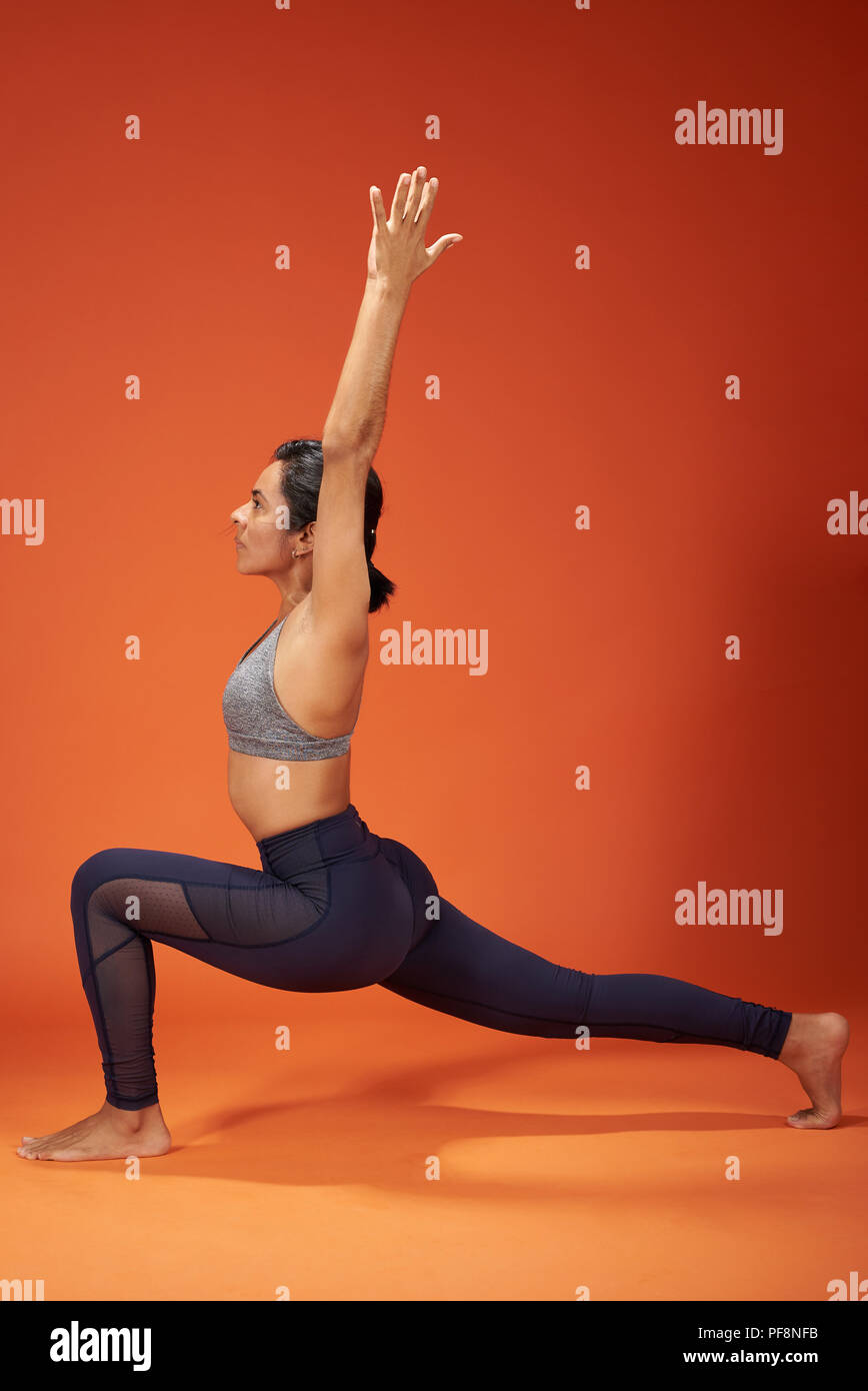 Affondo della scimmia yoga pone donna visualizza il colore arancione studio backgrpound Foto Stock