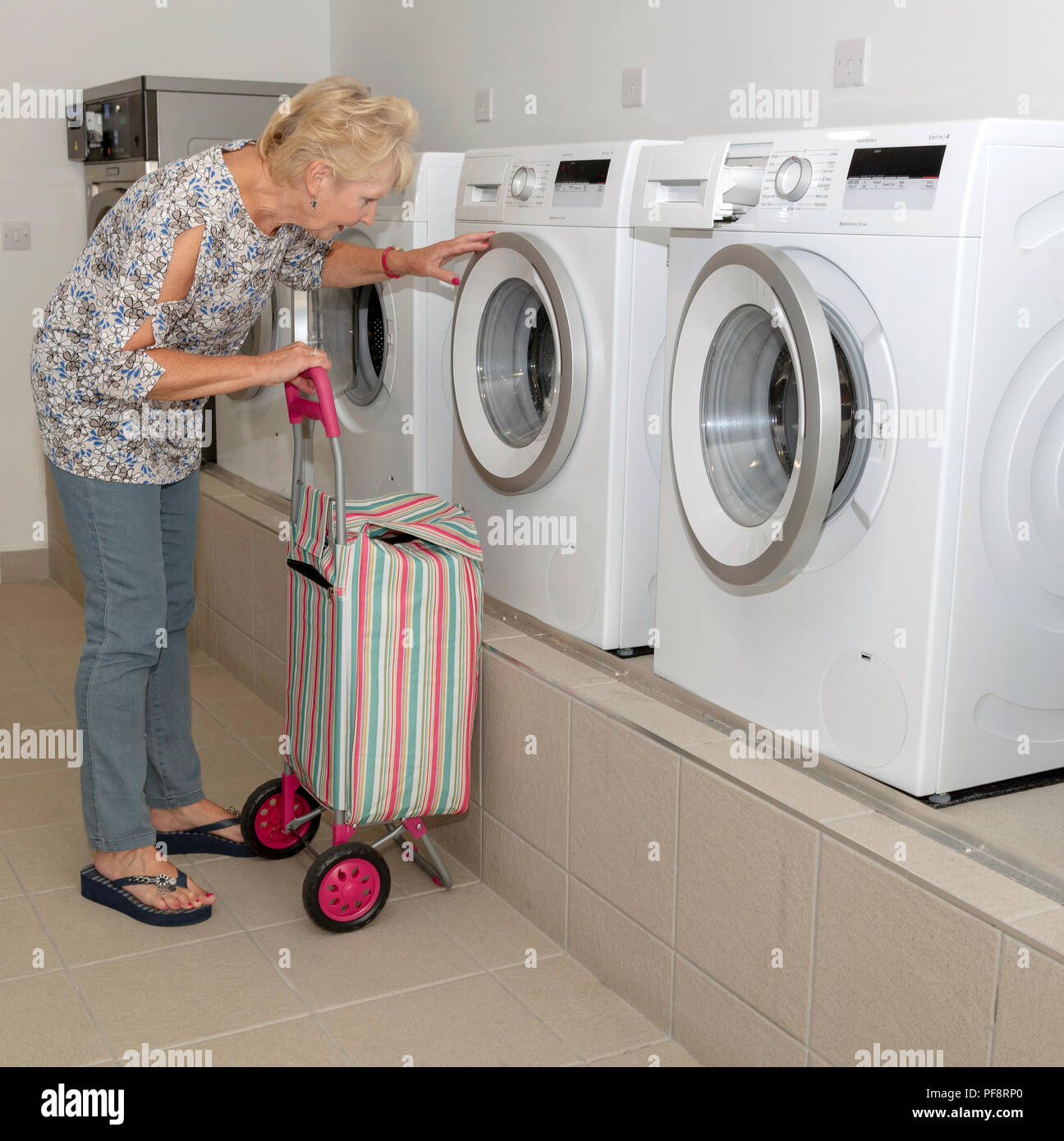 Donna anziana con la sua sporca carrello Lavaggio di controllo della macchina di lavaggio in una sala lavanderia Foto Stock