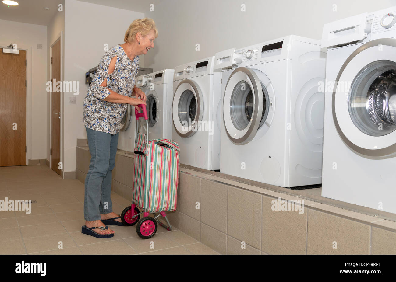 Donna anziana con la sua sporca carrello Lavaggio di controllo della macchina di lavaggio in una sala lavanderia Foto Stock