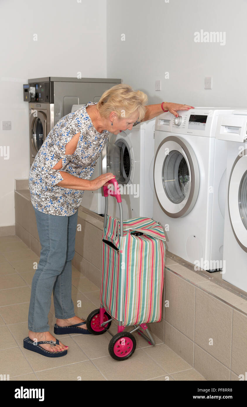 Donna anziana con la sua sporca carrello Lavaggio di controllo della macchina di lavaggio in una sala lavanderia Foto Stock