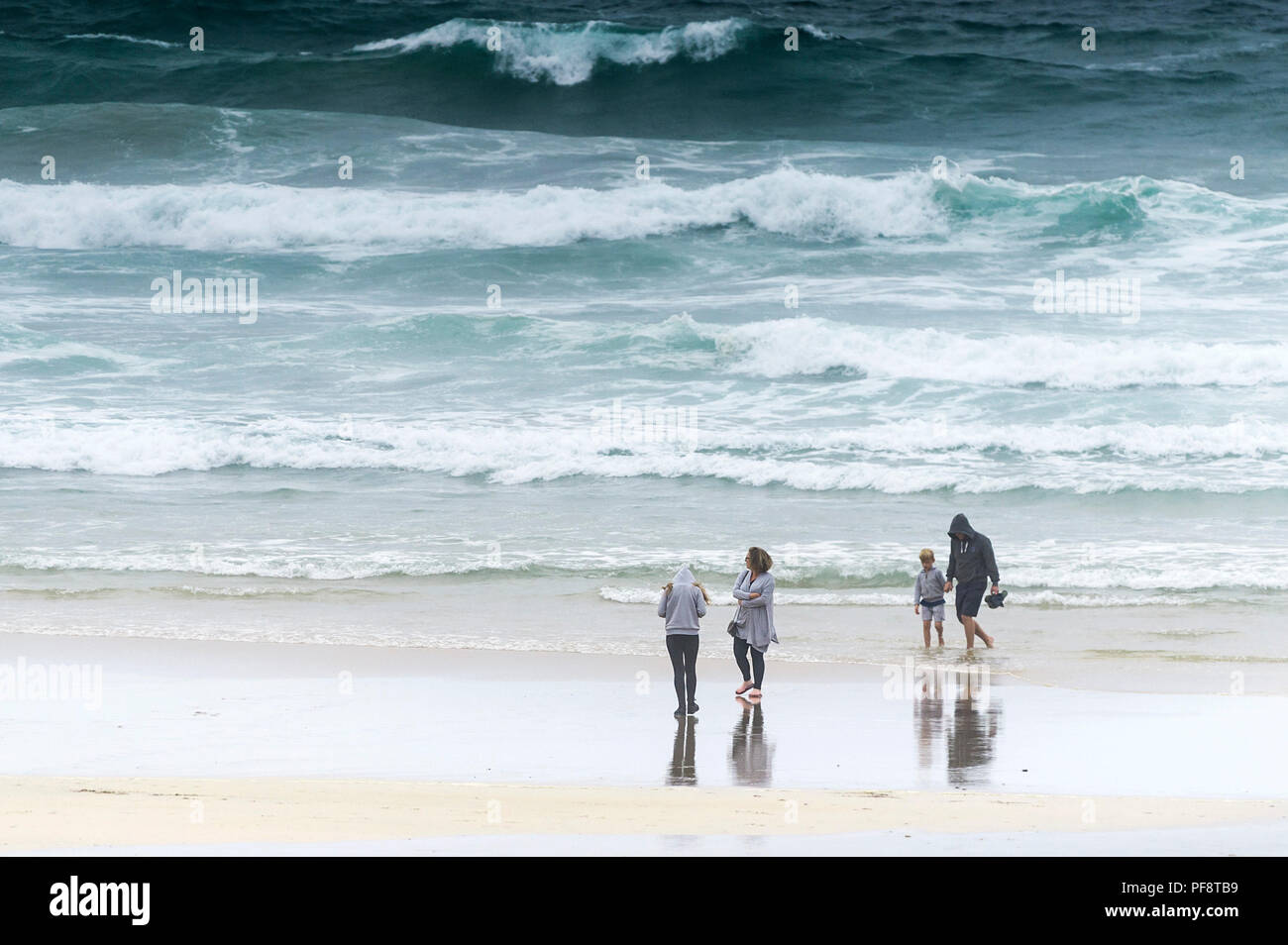 Una famiglia passeggiando sulla battigia a Fistral Beach in una fredda giornata grigia. Foto Stock