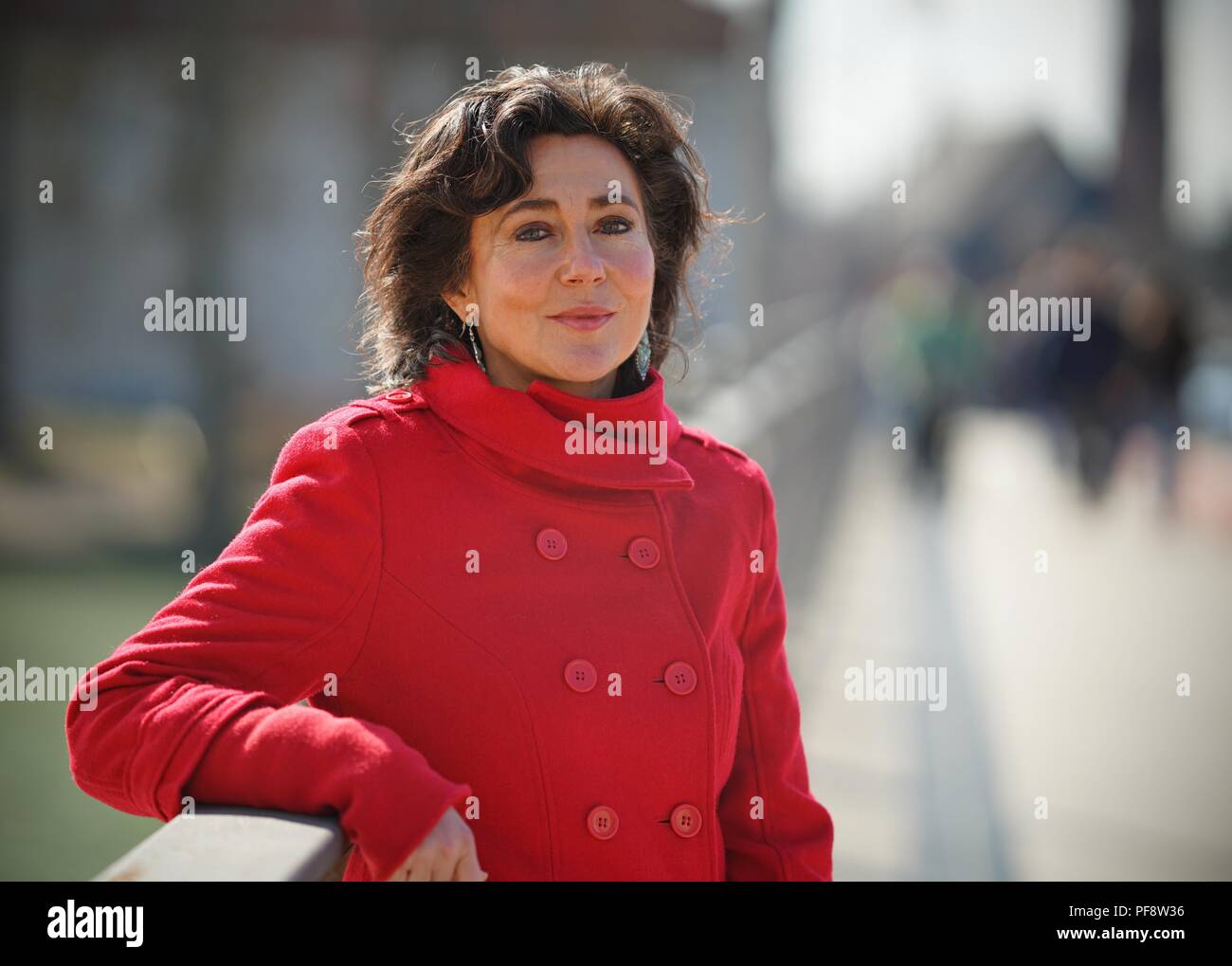 Woman in Red coat su un brigdge, età 44-55, sorridente, sfondo sfocato Foto Stock