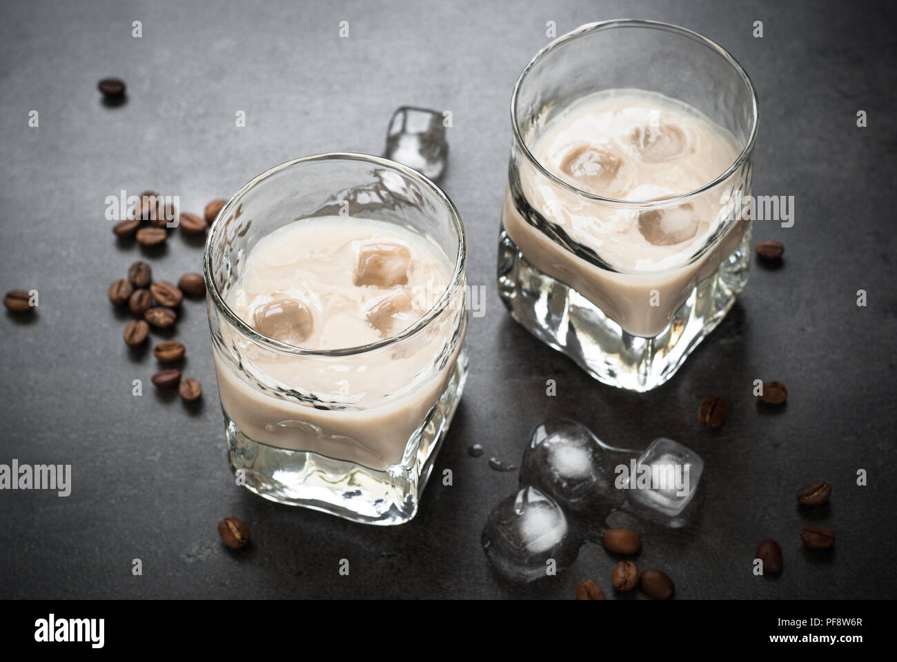 Liquore al caffè in bicchieri di ghiaccio e i chicchi di caffè sulla tavola nera. Foto Stock