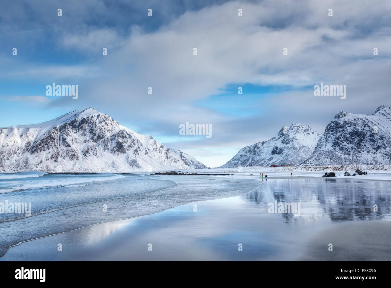 Montagne innevate e cielo blu con nuvole riflettono in acqua in inverno. Arctic spiaggia sabbiosa in isole Lofoten in Norvegia. Paesaggio con rocce, mare, peopl Foto Stock