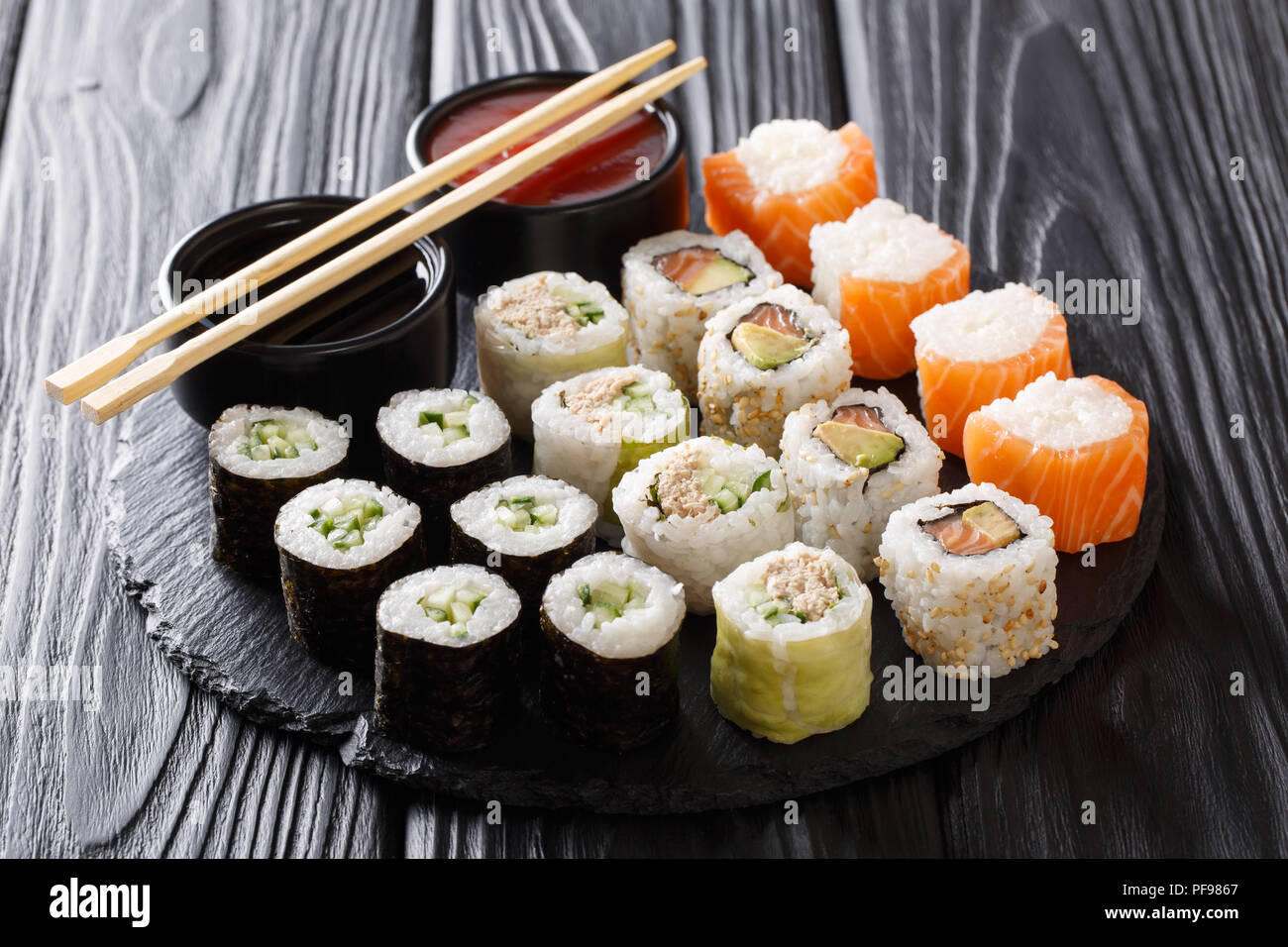 Rotoli di Sushi set con salse servito su nero ardesia pietra su sfondo scuro. Posizione orizzontale Foto Stock