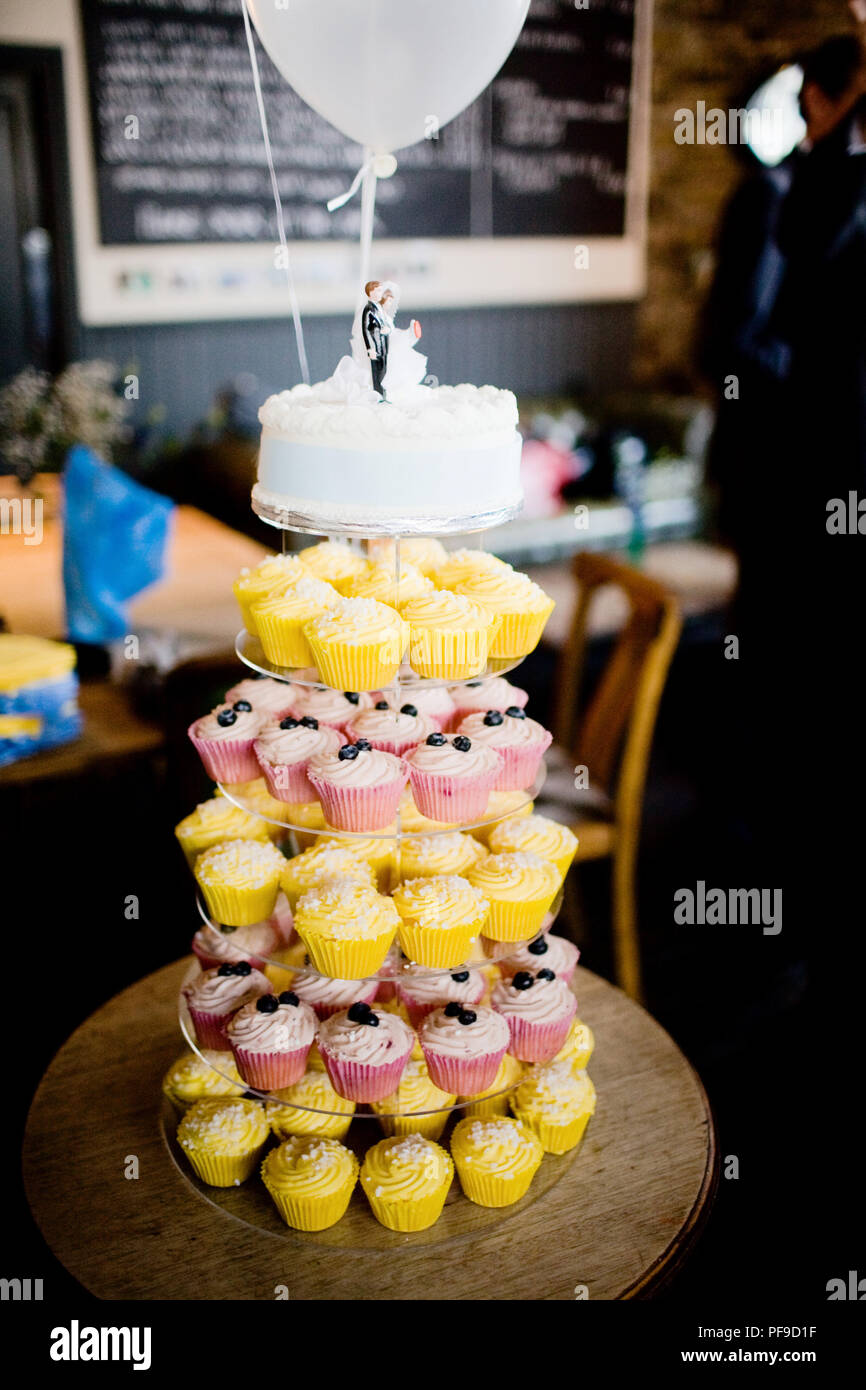 Moderna torta di nozze con livelli di una torta con tortine e la sposa e lo sposo statuetta in un pub impostazione Foto Stock