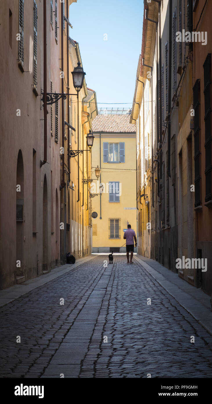 Un uomo e il suo cane, passeggiate attraverso la soleggiata acciottolati vicoli della città di Piacenza, Italia, Europa. Foto Stock