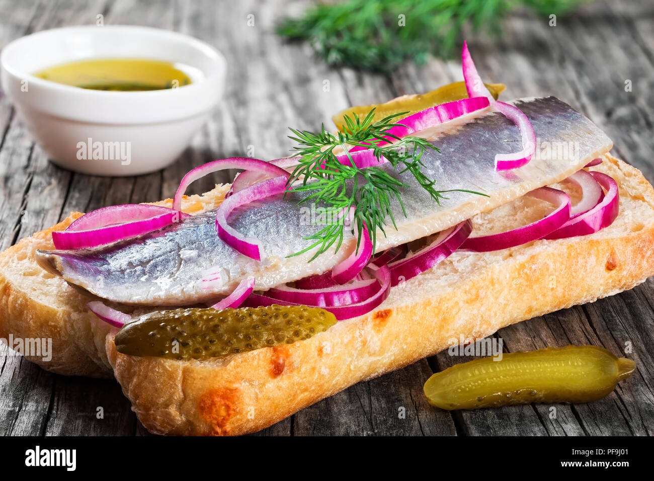 Sandwich CON FILETTI DI ARINGHE, cipolla, cetriolo sottaceto e aneto su carta pergamena su un ovale piatto su un vecchio tavolo rustico e tradizionale cibo di strada in Foto Stock