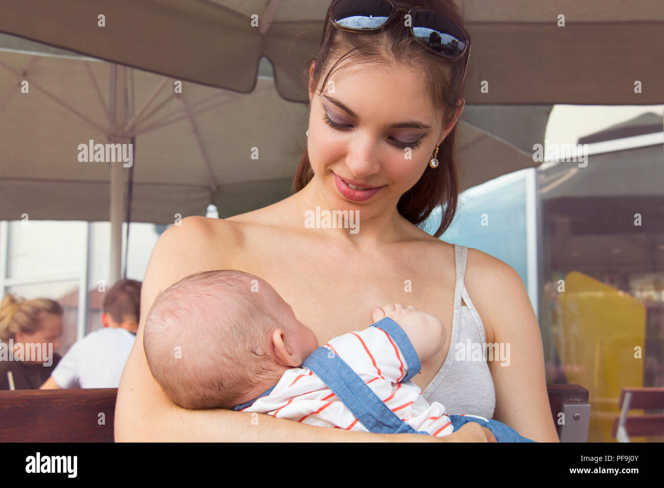 Felice madre allattamento neonato in luogo pubblico, donna con faccia allegra tenendo poco infantile al di fuori, bella signora sorridente al suo grazioso baby Foto Stock
