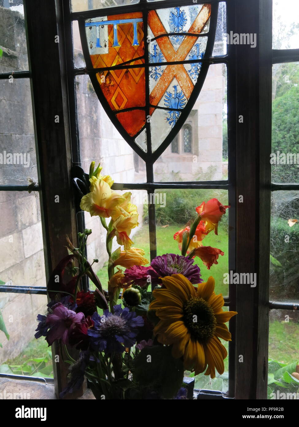 Vista attraverso la finestra alla proprietà del National Trust, Baddesley Clinton; vetrate in cresta i vetri dei finestrini e in estate i fiori sul davanzale. Foto Stock