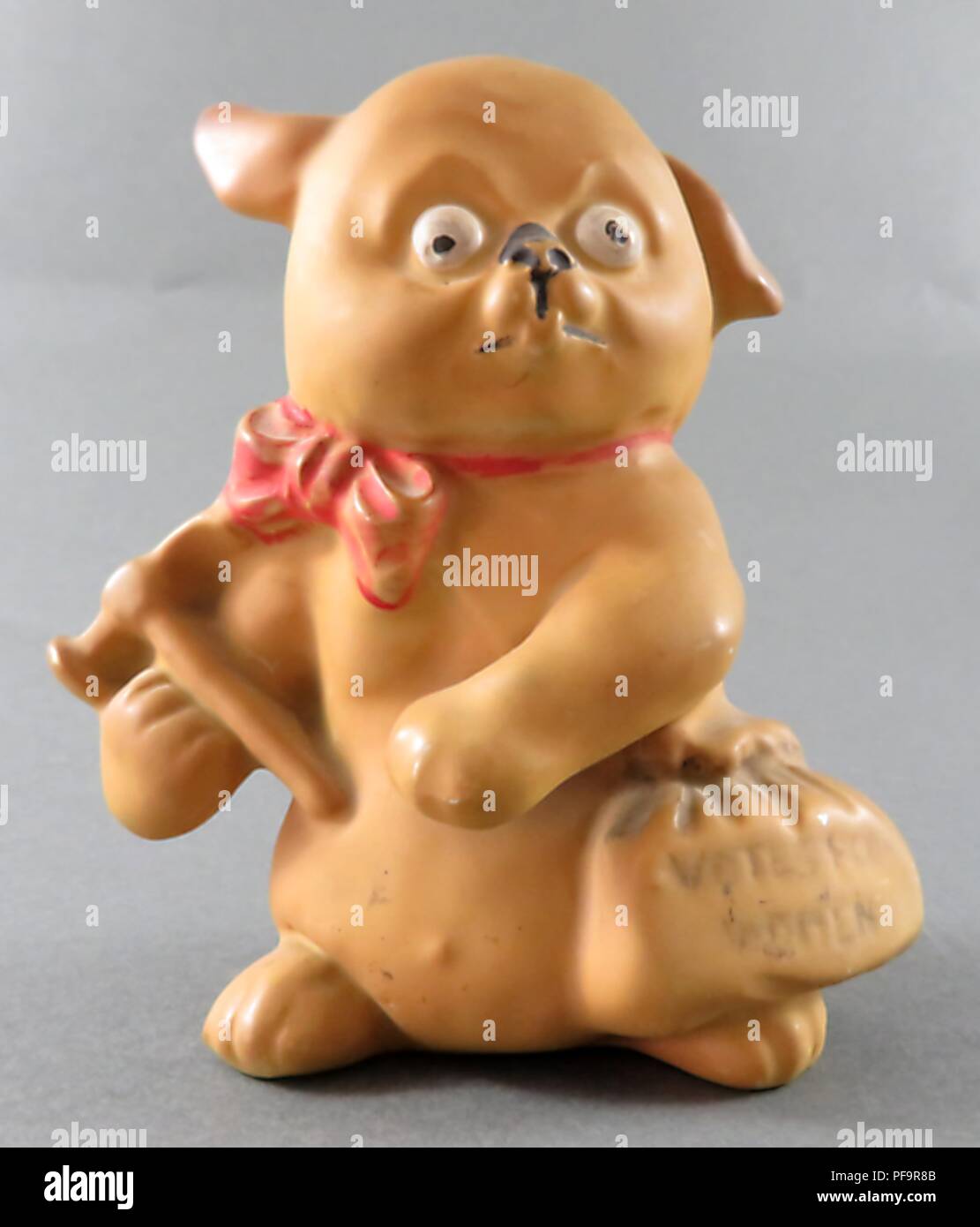 Statuetta in ceramica raffigurante un cane, in piedi sulle zampe posteriori, indossando un fiocco rosso cravatta, con una espressione di allarme sulla sua faccia, un sacchetto con la dizione "voti per le donne nella sua vita e un martello in una mano, alludendo all'inglese suffragists rompendo le vetrine in segno di protesta, 1900. () Foto Stock