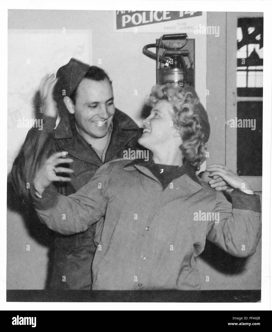 Fotografia in bianco e nero, mostrando un uomo dietro una bionda donna, entrambi in tre quarti di lunghezza vista, indossano uniformi militari e di stare al chiuso nella parte anteriore di un estintore, l'uomo regola il suo cappello con una mano mentre l'altra sua mano è sul alle spalle della donna, la donna guarda indietro e sorrisi a lui, probabilmente fotografato durante la II Guerra Mondiale, 1945. () Foto Stock