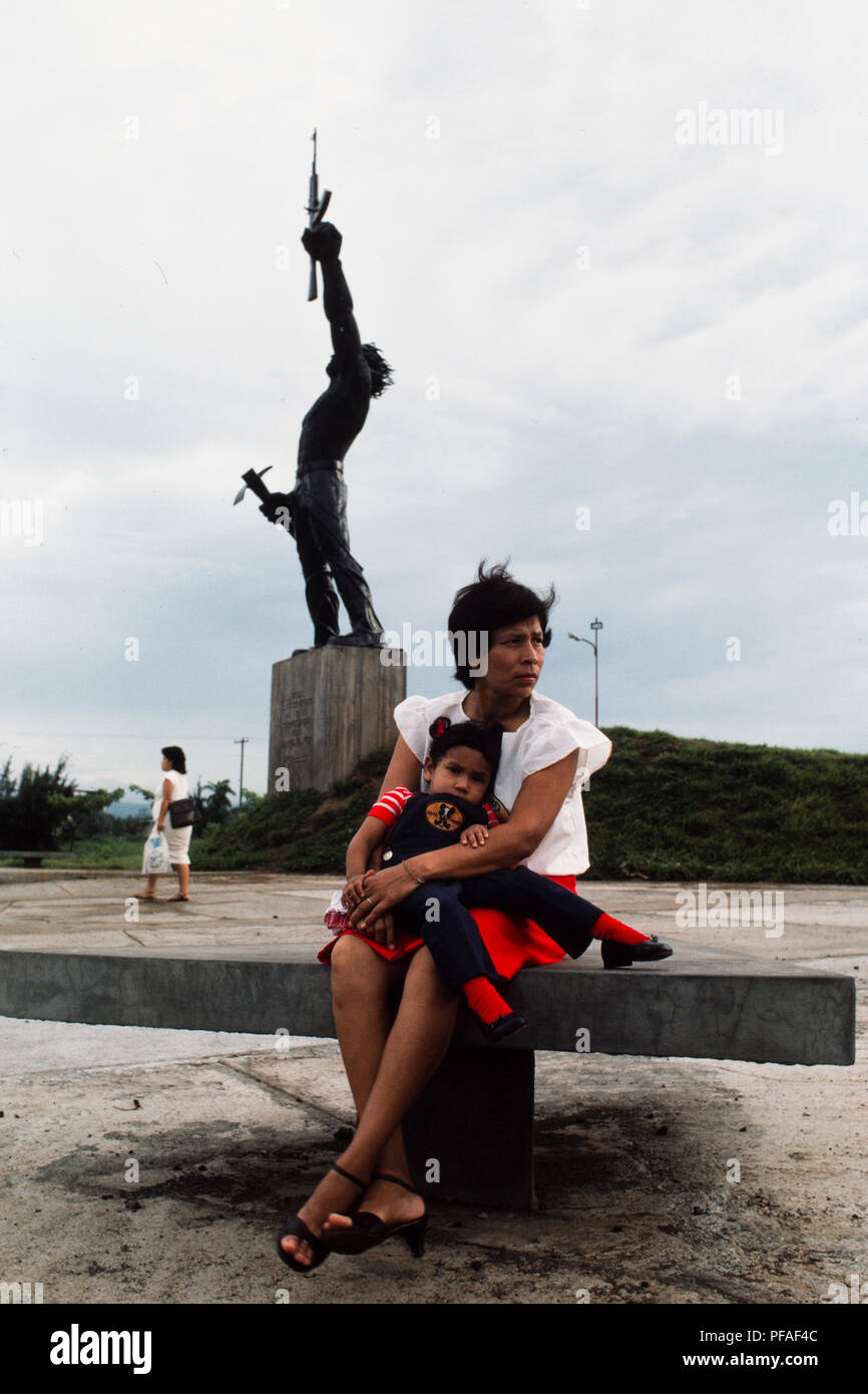 Managua, Nicaragua, giugno 1986; una donna e suo figlio in attesa in un parco nel centro di Managua accanto a un governo FSLN statua a eroi della rivoluzione. ' Foto Stock