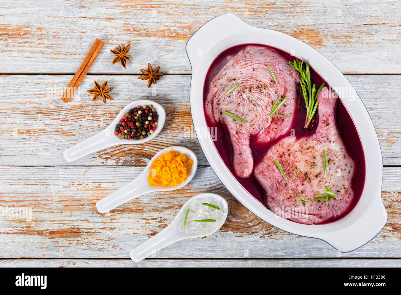 Materie duck gambe la preparazione per la tostatura marinato nel vino brulé con spezie, il rosmarino e la scorza di arancia in posizione gratin piatto su peeling schede di vernice, vista dal Foto Stock