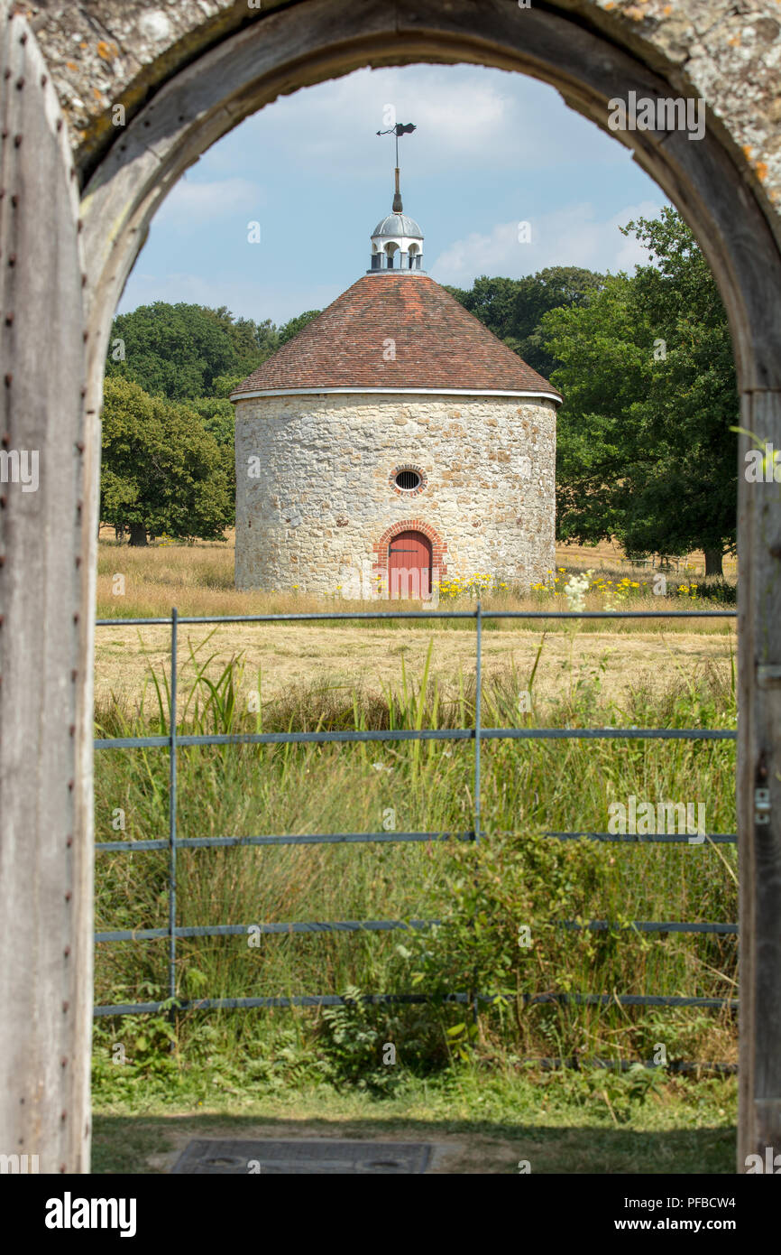Storico in pietra circolare di macerie colombaia in motivi di Parham House, Pulborough, West Sussex, visto da Parham giardini. Foto Stock