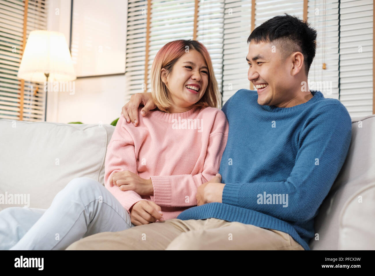 Asian giovane abbracciando e ridere mentre è seduto al divano in casa.amante matura nel concetto di casa Foto Stock