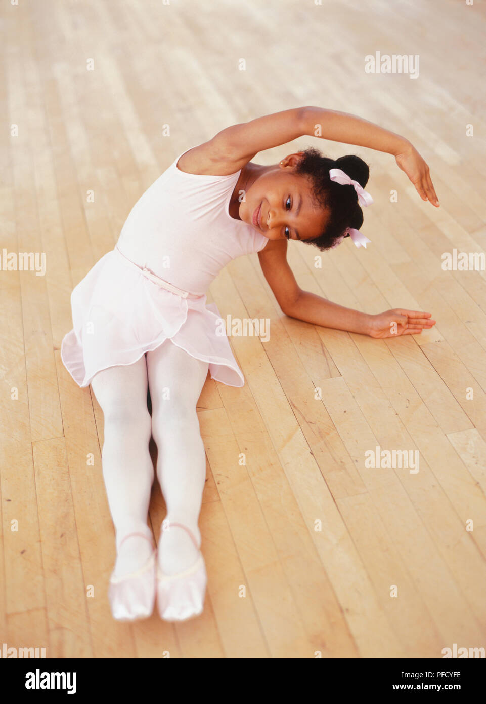 Giovane ballerina seduta sul pavimento, gambe dritte, le braccia sopra la testa e tenuto a lato. Foto Stock
