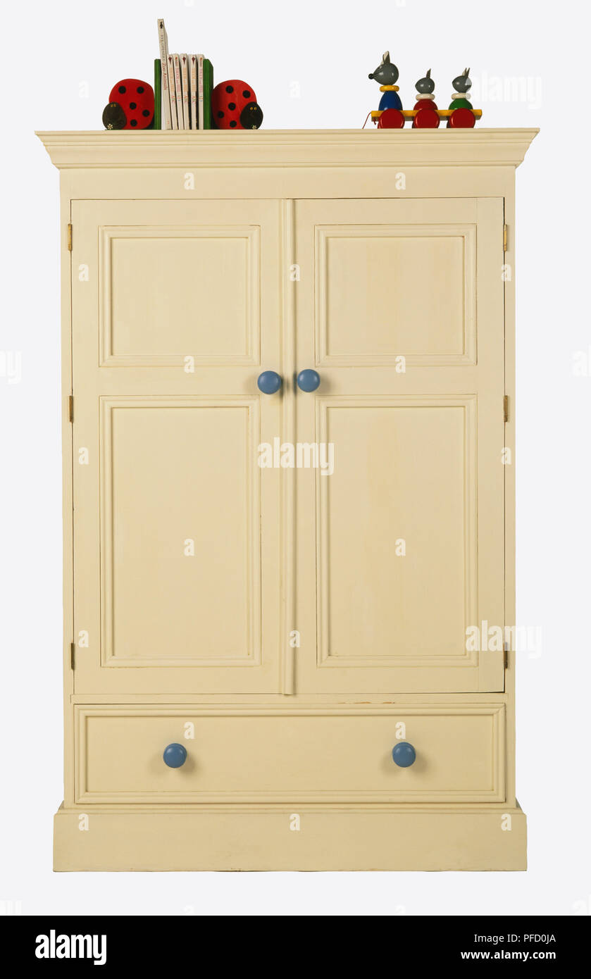 La crema doppio armadio con manopole blu e cassetto singolo in fondo, giocattoli colorati in cima, vista frontale. Foto Stock