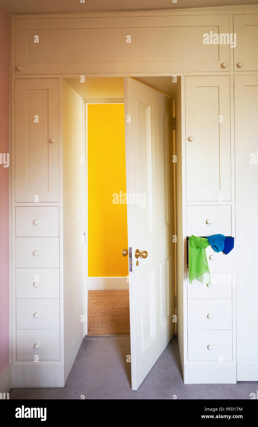 Built-in bianco unità guardaroba incorniciare una porta bianca si apre ad una sala con pareti dipinte di un giallo. Foto Stock