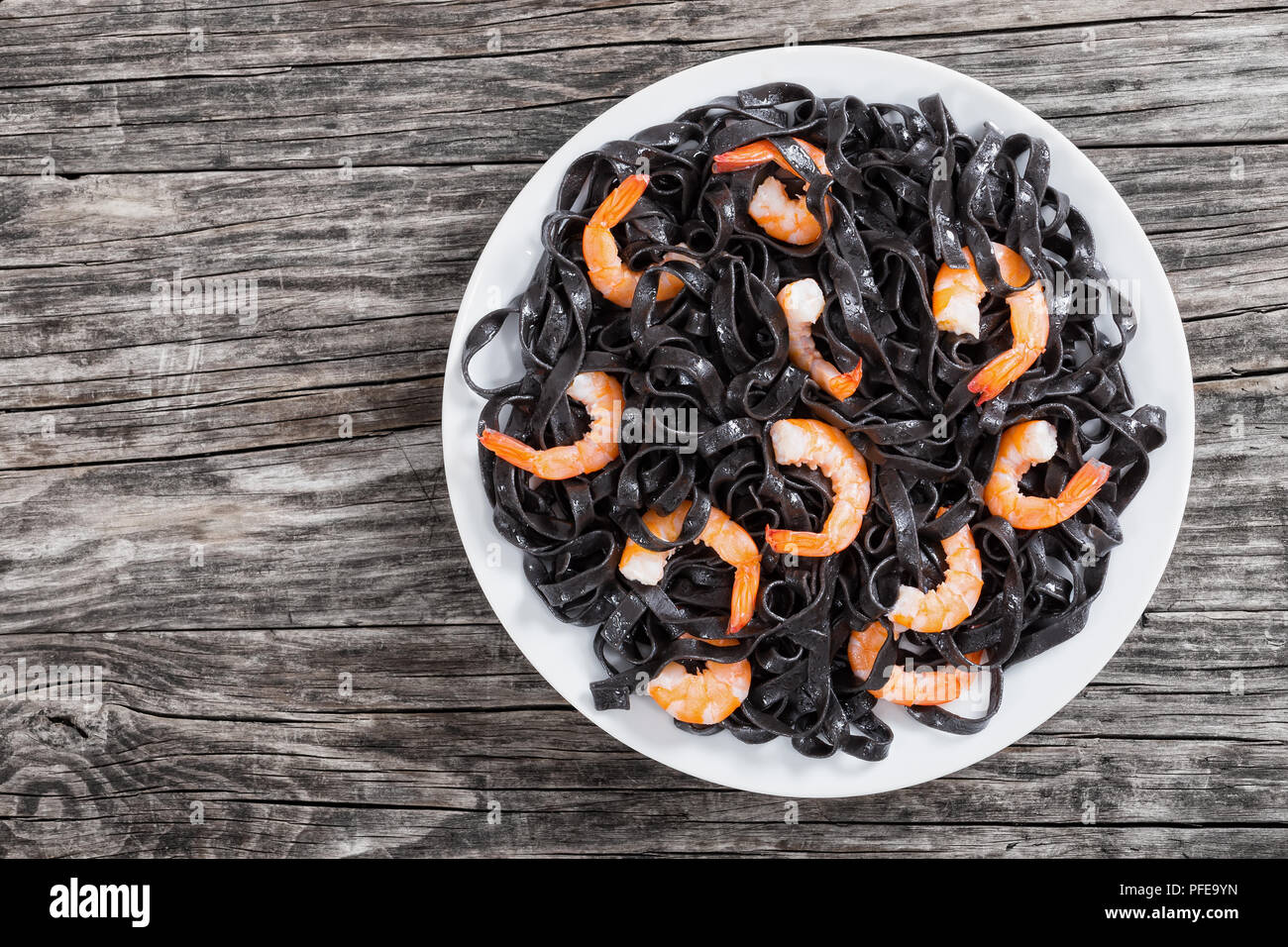 Deliziosa nero di seppia tagliatelle nere con gamberetti sul piatto bianco sul buio wwoden tabella, vista dall'alto. Foto Stock