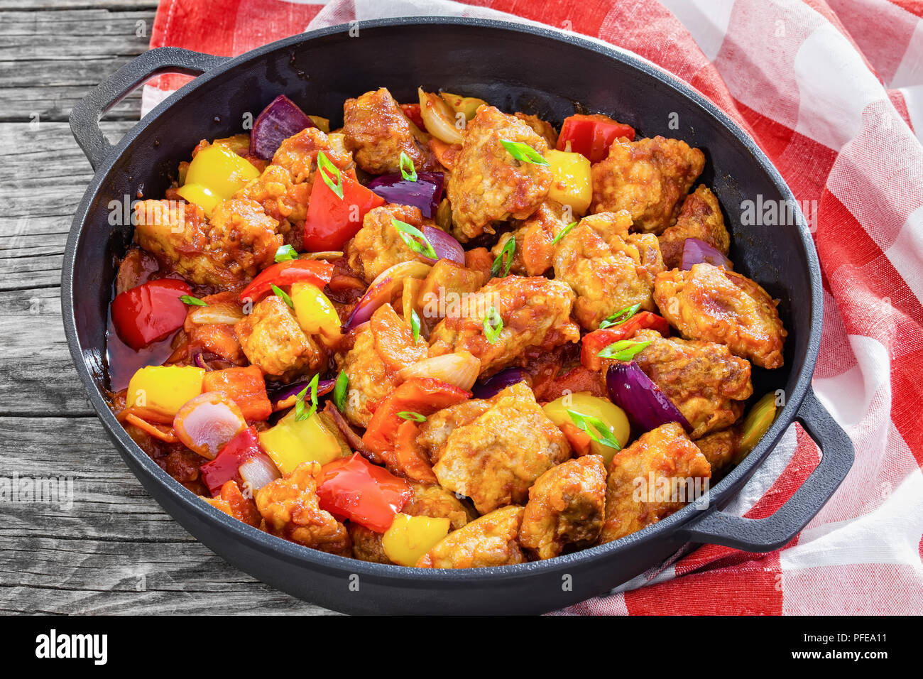 Dolce e aspro fritti bocconcini di maiale con verdure, cosparsi di cipolla verde nella casseruola di ferro sul legno scuro dello sfondo con carta asciugatutto , tradizione Foto Stock