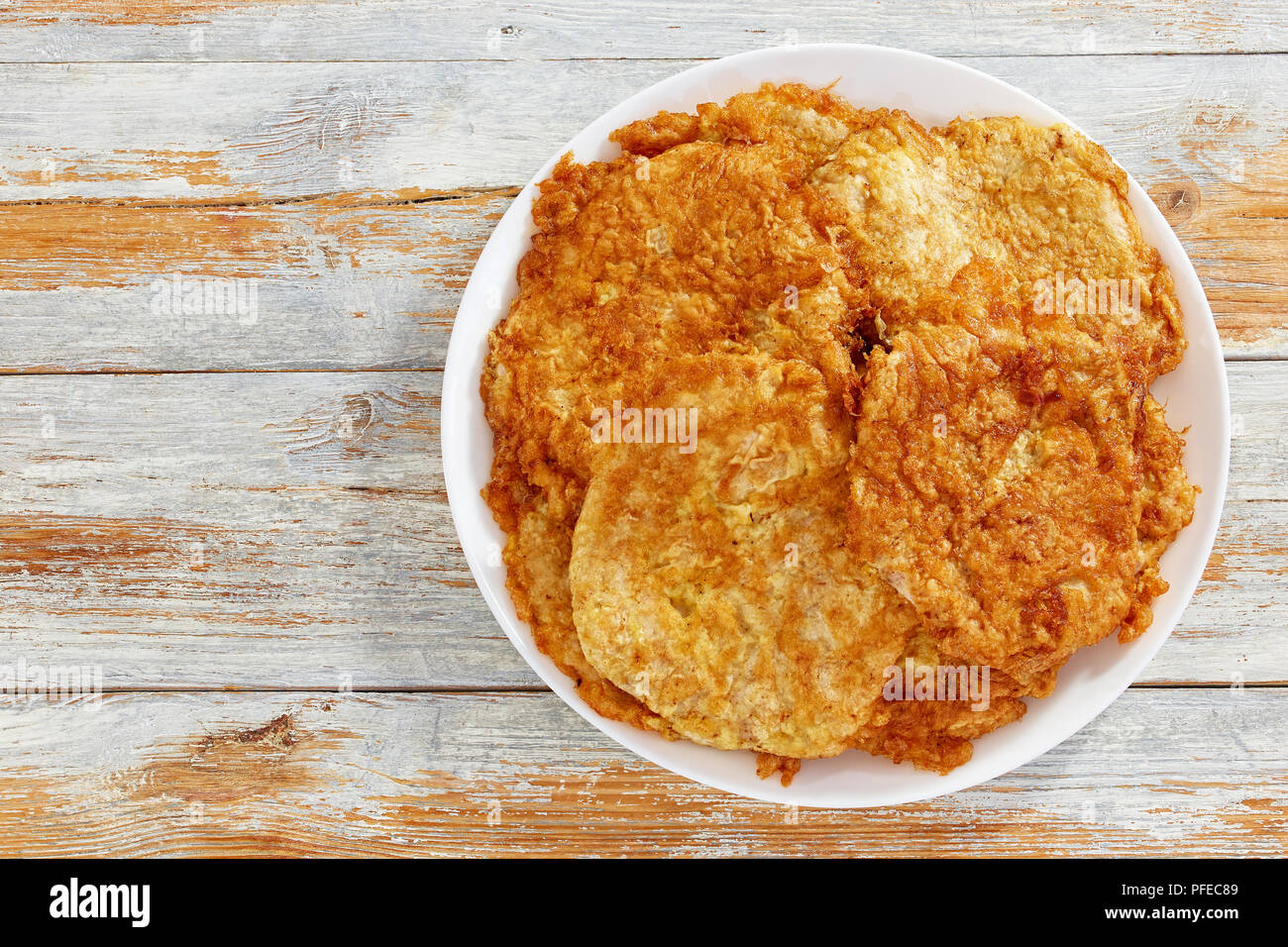 Deliziosi fritti in pastella impanata disossate costolette di maiale sul piatto bianco sul vecchio tavolo in legno, vista da sopra Foto Stock