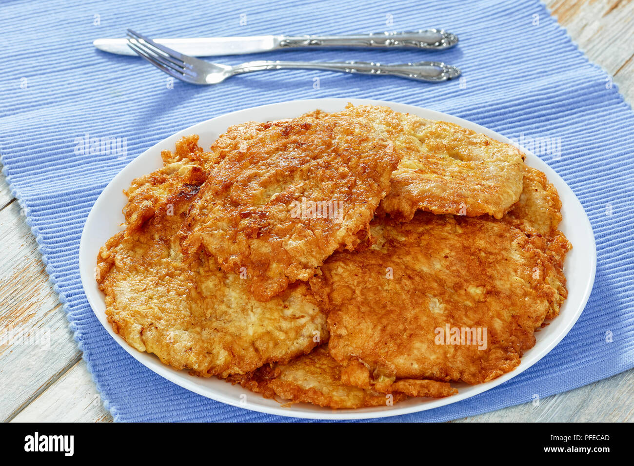 Oven-Fried costolette di carne sul piatto bianco sulla tabella MAT con coltello e forchetta, sul vecchio sfondo di legno, facile ricetta italiana, vista da sopra, close-up Foto Stock