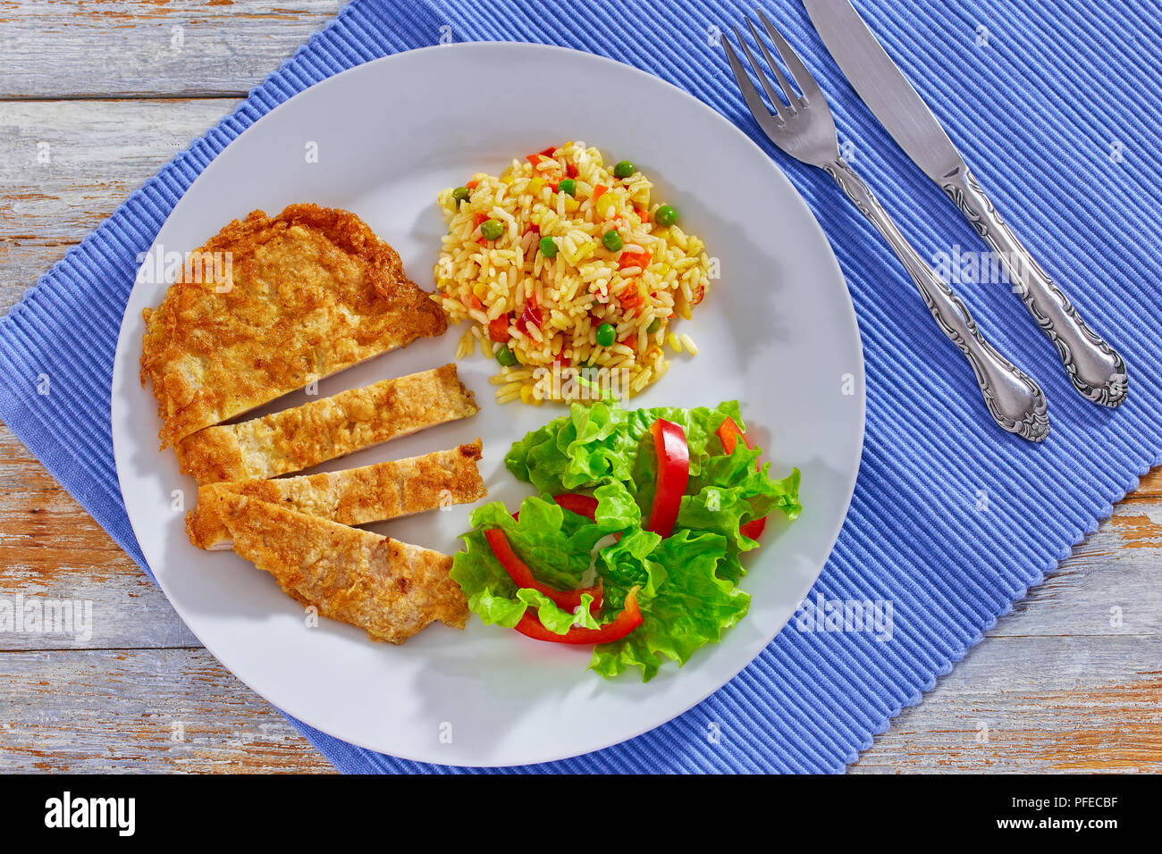 Paese fritto costolette di maiale tagliata in strisce con colorati risotti e lattuga fresca bell pepper salad sulla piastra bianca sulla tabella MAT, close-up, vista da abov Foto Stock