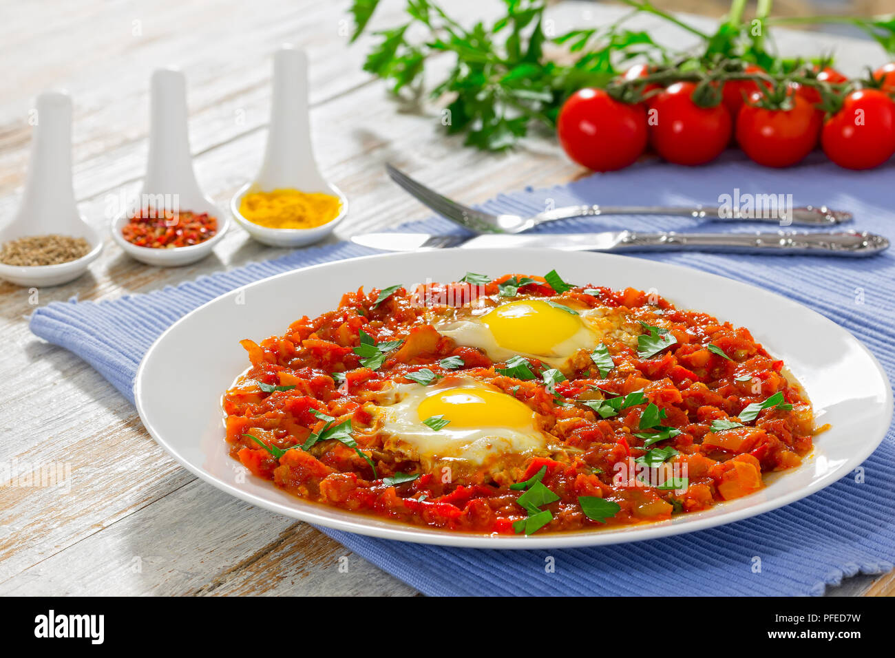 Sunny Side fino le uova con verdure cosparsa di prezzemolo o shakshuka - peperone, peperoncino, pomodoro sul piatto bianco sulla tabella MAT. Spezie, ciliegia tomat Foto Stock