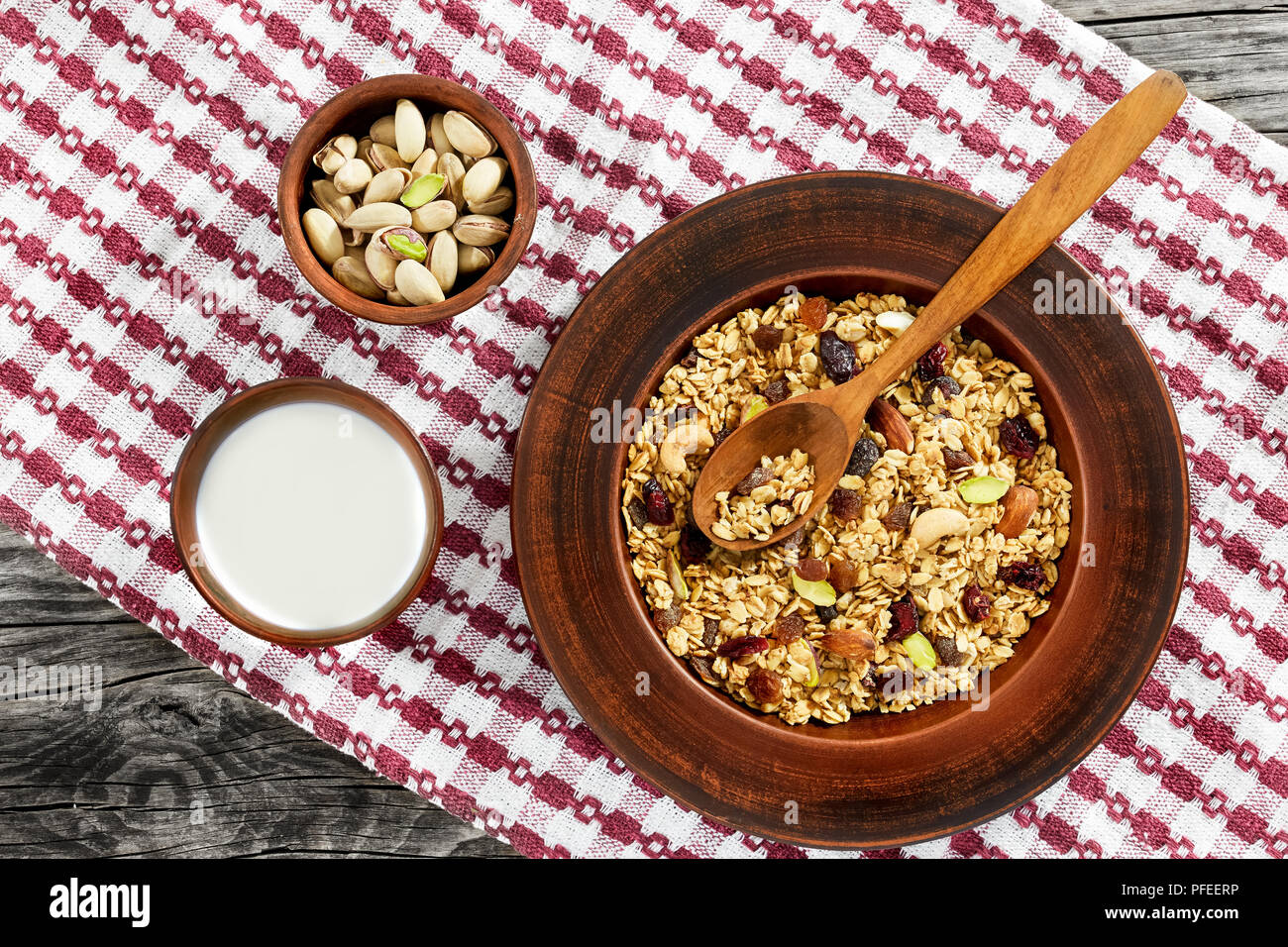 Una sana prima colazione - granola con miele, farina di avena, anacardi, mandorle, pistacchi, uva passa e mirtilli secchi nel piatto di argilla, tazza di yogurt e ciotola con n Foto Stock