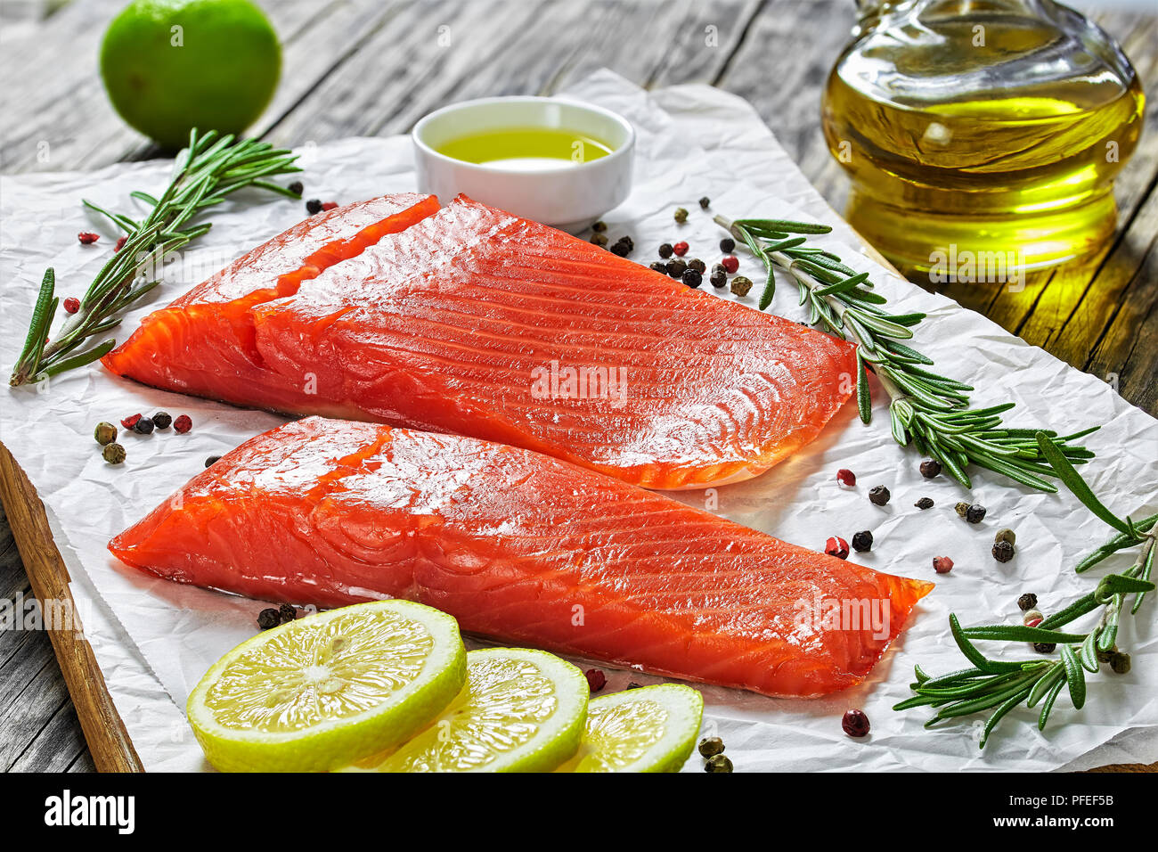 Due pezzi di salmone salato filetto di pesce con rosmarino fresco, mix di pepe, olio nel sugo barca sul tagliere su carta, close-up Foto Stock