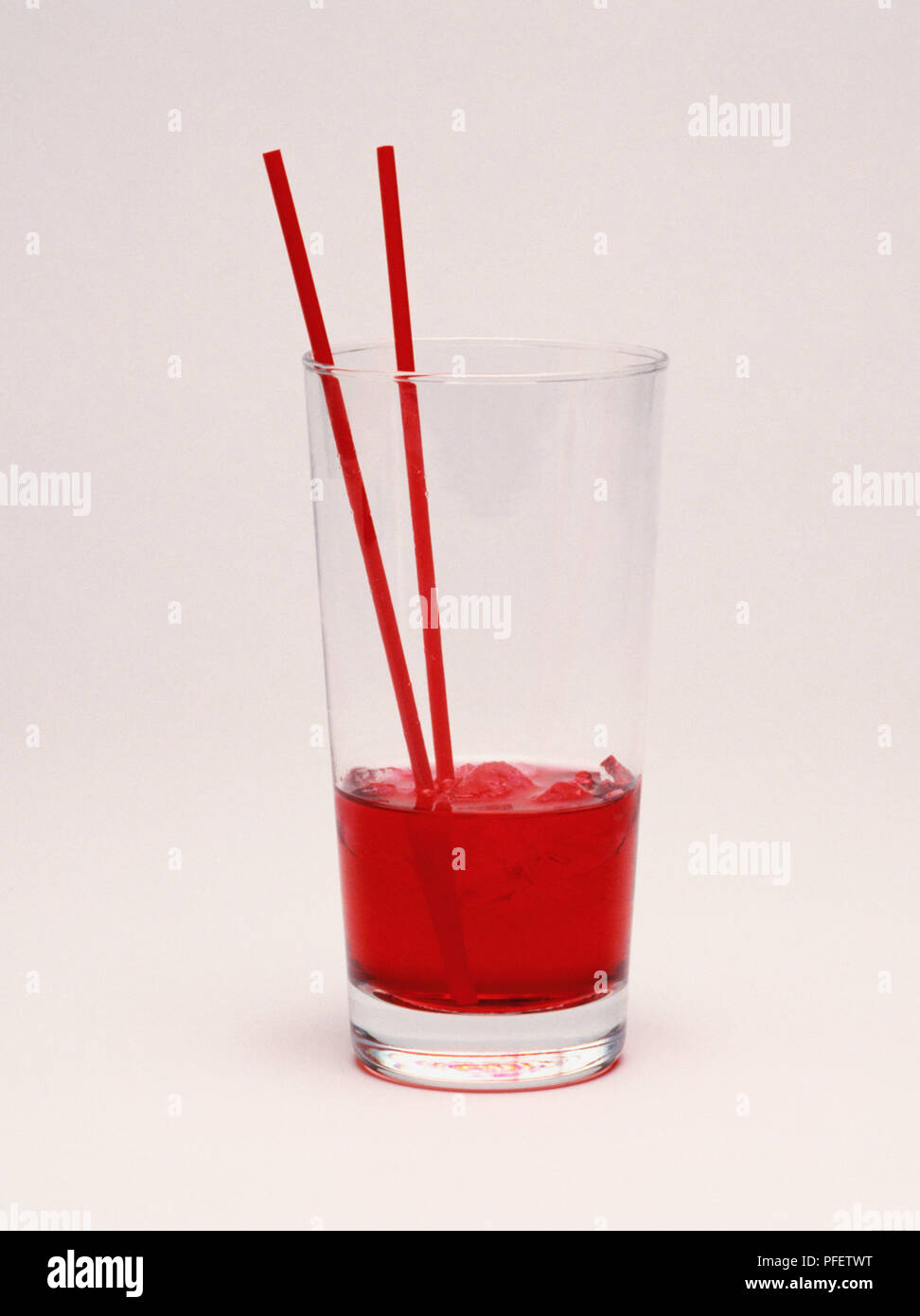 Bicchiere alto, terzo pieno di colore rosso e bevanda ghiacciata, due cannucce di rosso. Foto Stock