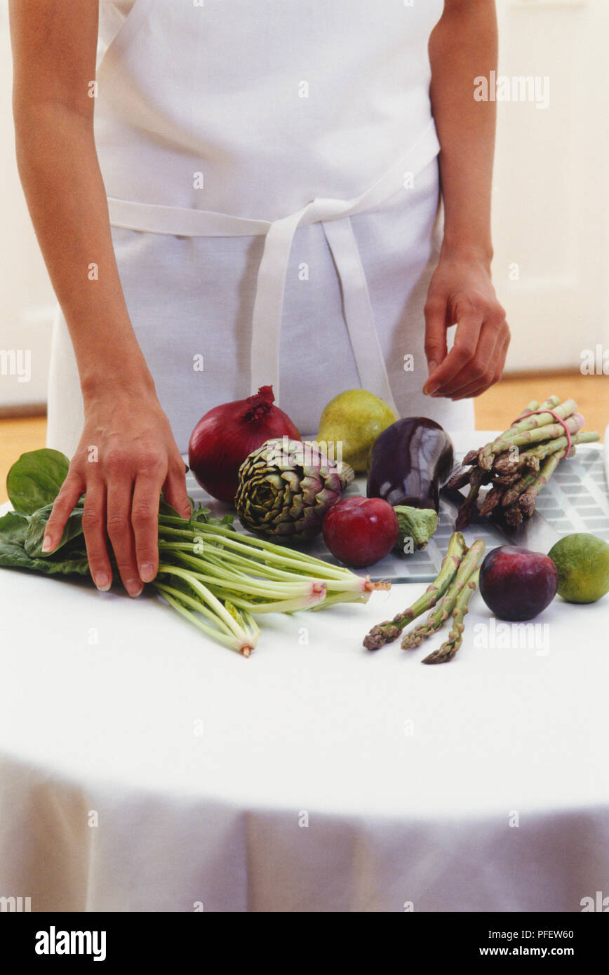 La donna la manipolazione di spinaci freschi sulla superficie di lavoro accanto alla varietà di frutta e verdura Foto Stock