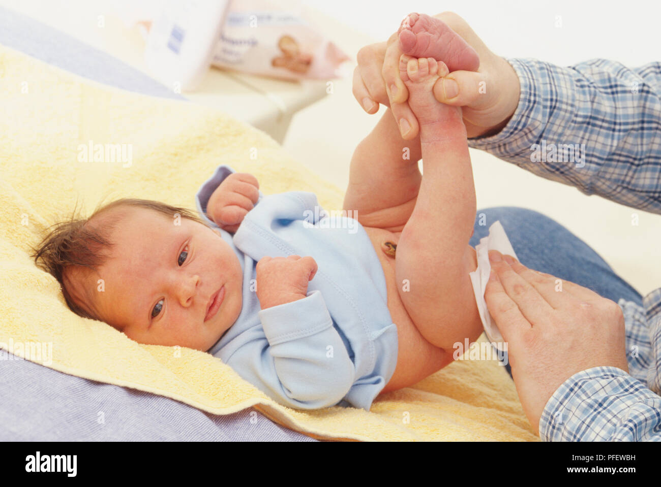 Baby boy stare sdraiato sulla schiena sul fasciatoio, maglietta tirata, uomo azienda baby per le gambe fino a piedi e strofinando il suo fondo con un panno morbido. Foto Stock