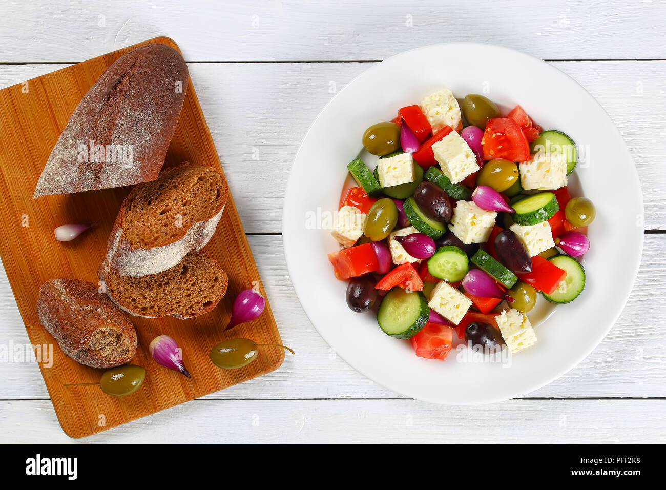 Deliziosa insalata greca con verdure fresche, il formaggio feta verde e olive kalamata, cipolla rossa lampadine su piastra bianca sulla tavola con crostini di pane casereccio Foto Stock