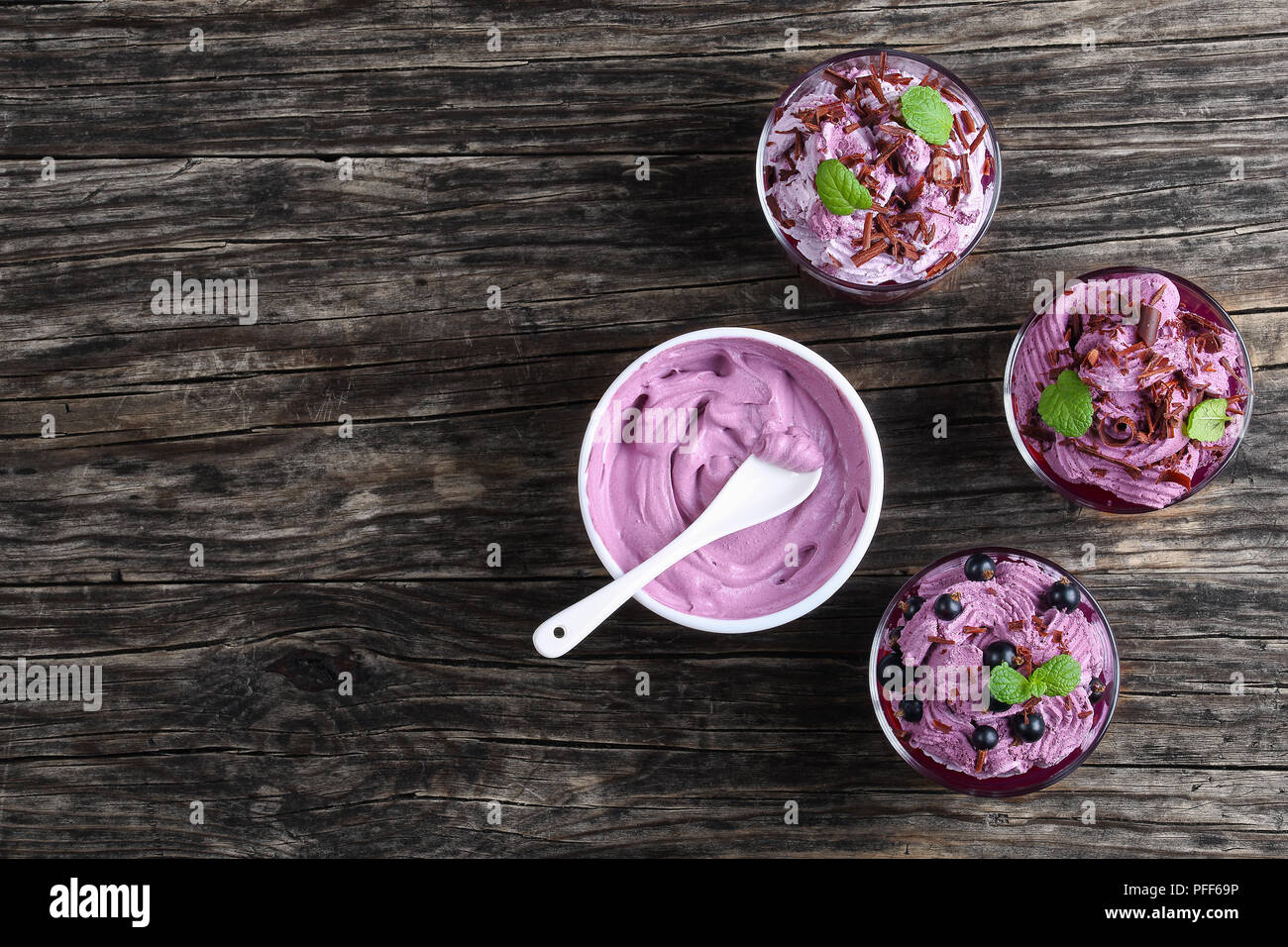 Sana deliziosi dessert estivo di ribes nero decorato con foglie di menta in bicchieri di vetro sul vecchio legno scuro tabella, congelate Panna ricotta Yogur Foto Stock