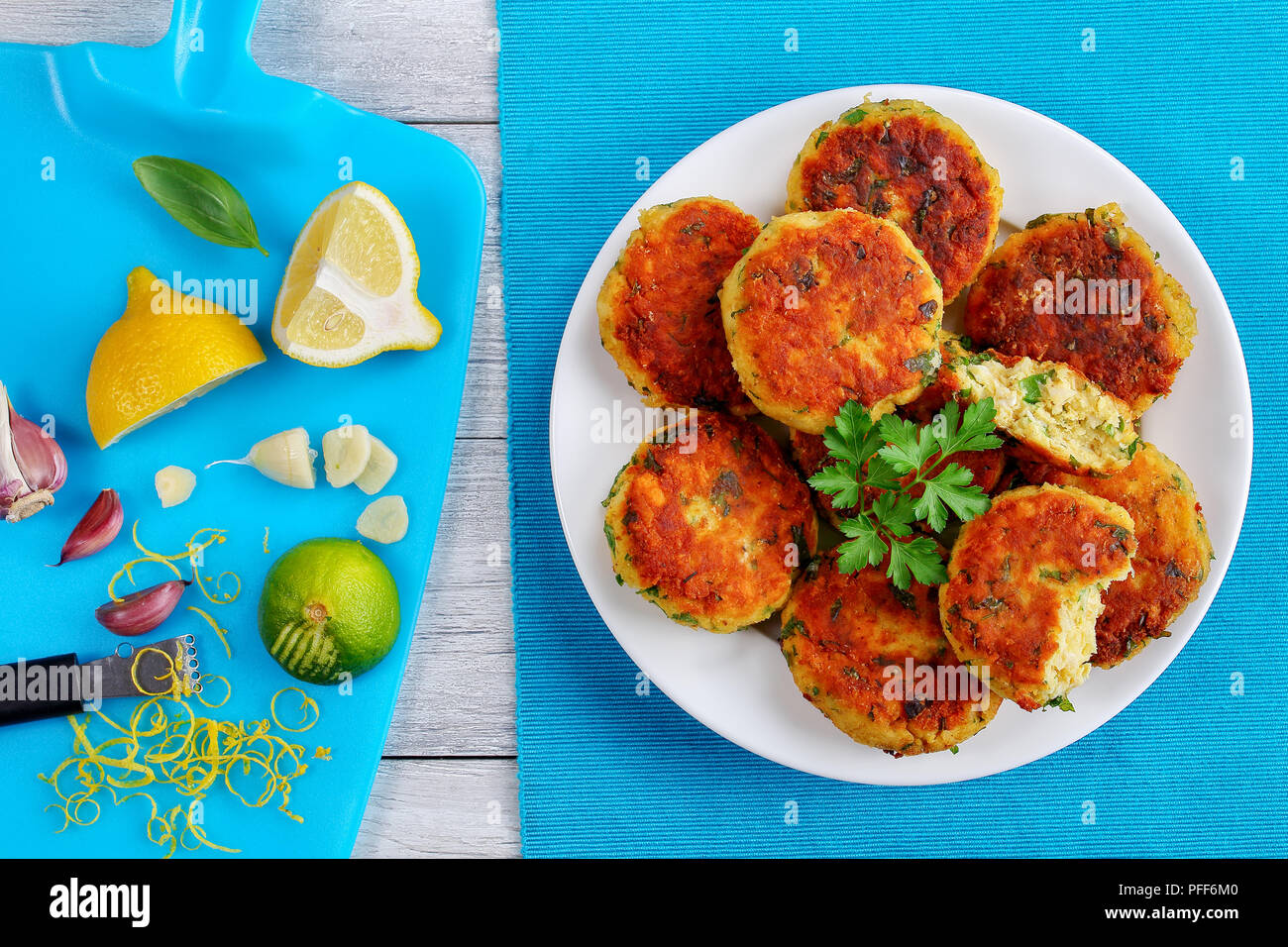 Freschi e deliziosi fritte fatte in casa Torte Pesce sulla piastra bianca con il prezzemolo sul vecchio tavolo in legno, spicchi di lime e limone sul bordo di taglio , ricetta classica, Foto Stock