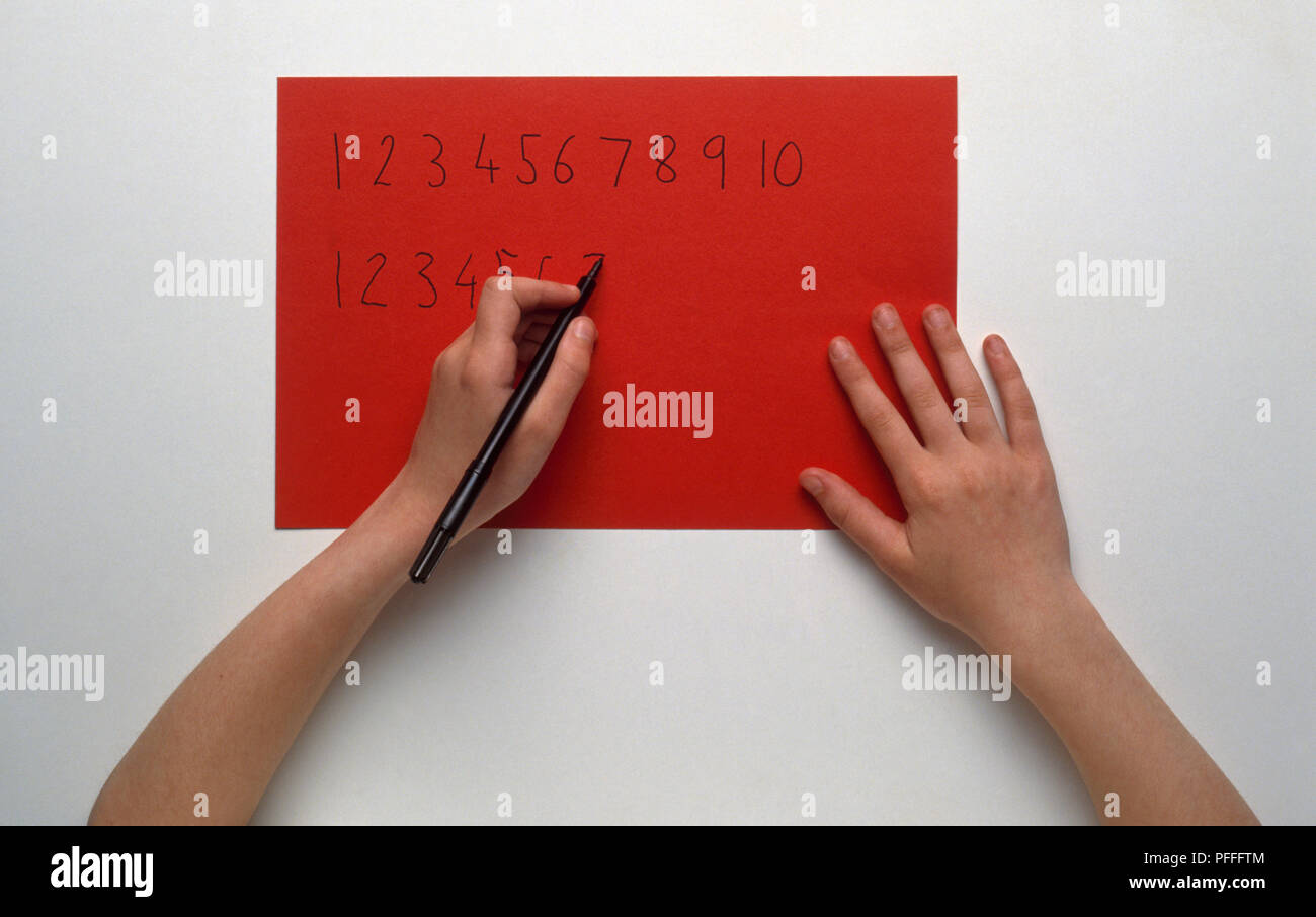 Bambino con mano sinistra a scrivere i numeri su carta rossa con nero pennarello Foto Stock