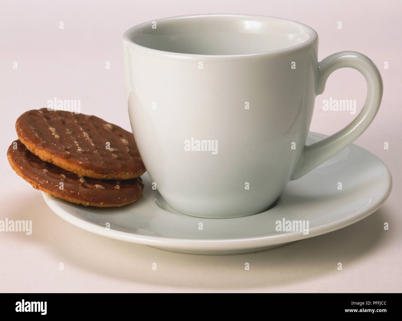 Tazza bianca con piattino con due biscotti al cioccolato in appoggio sul piattino, vista frontale. Foto Stock