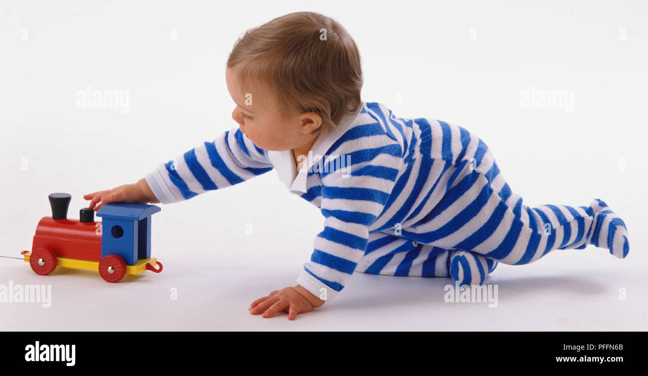 Il bambino che indossa blu e bianco tuta, sporgersi in avanti, afferrando colorato toy train. Foto Stock