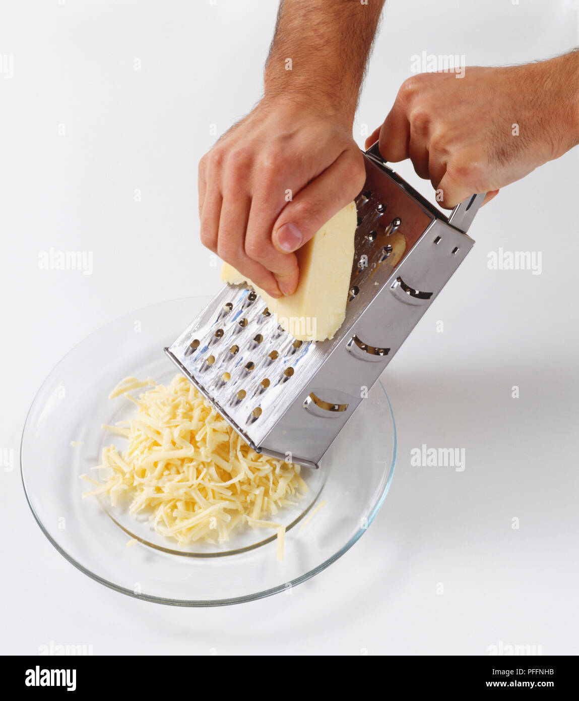 Utilizzando metallo grattugia manualmente per grattugiare il formaggio cheddar su una lastra di vetro chiara, ad alto angolo di visione Foto Stock