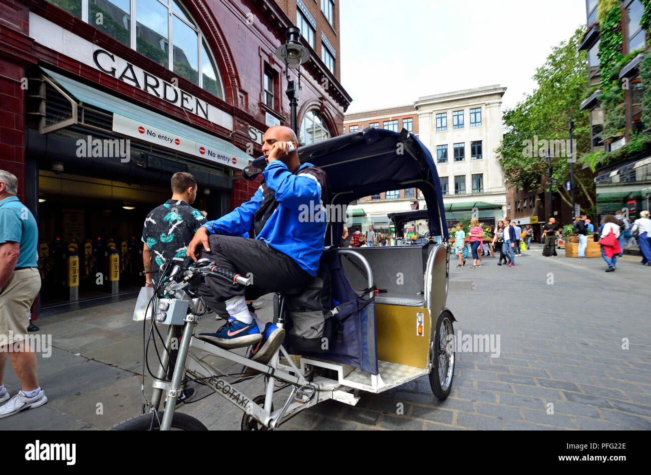 In rickshaw driver sul suo telefono cellulare da Covent Garden la stazione della metropolitana di Londra, Inghilterra, Regno Unito. Foto Stock