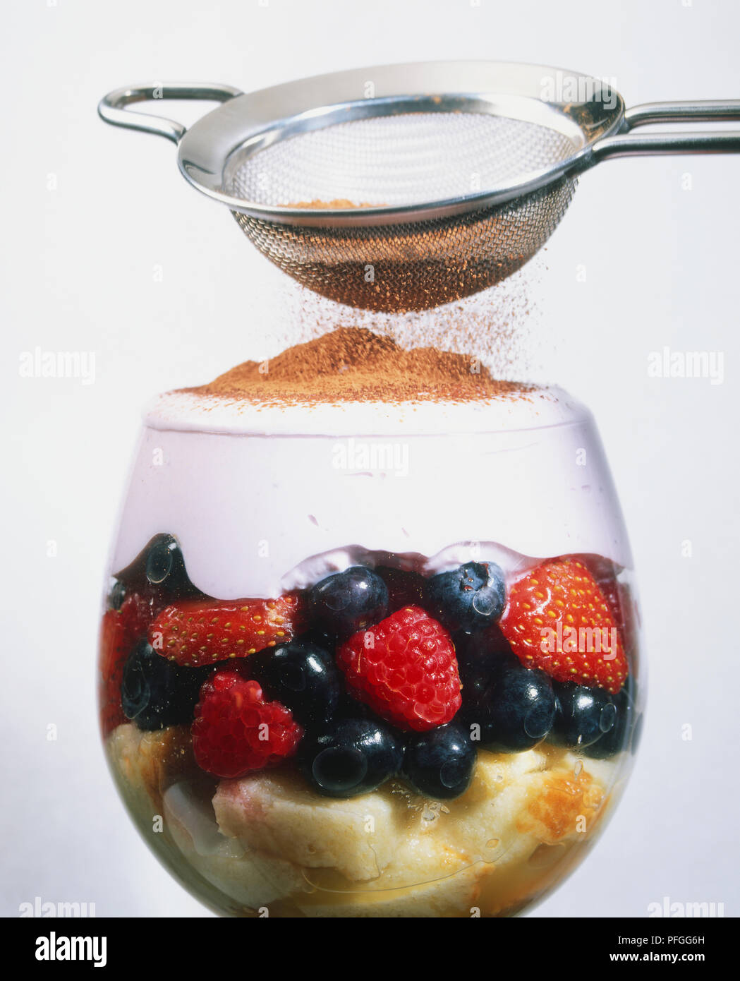 Spargendo cioccolata in polvere sulla crema topping di frutta ricotta dessert Tiramisu, servito in un bicchiere da vino Foto Stock