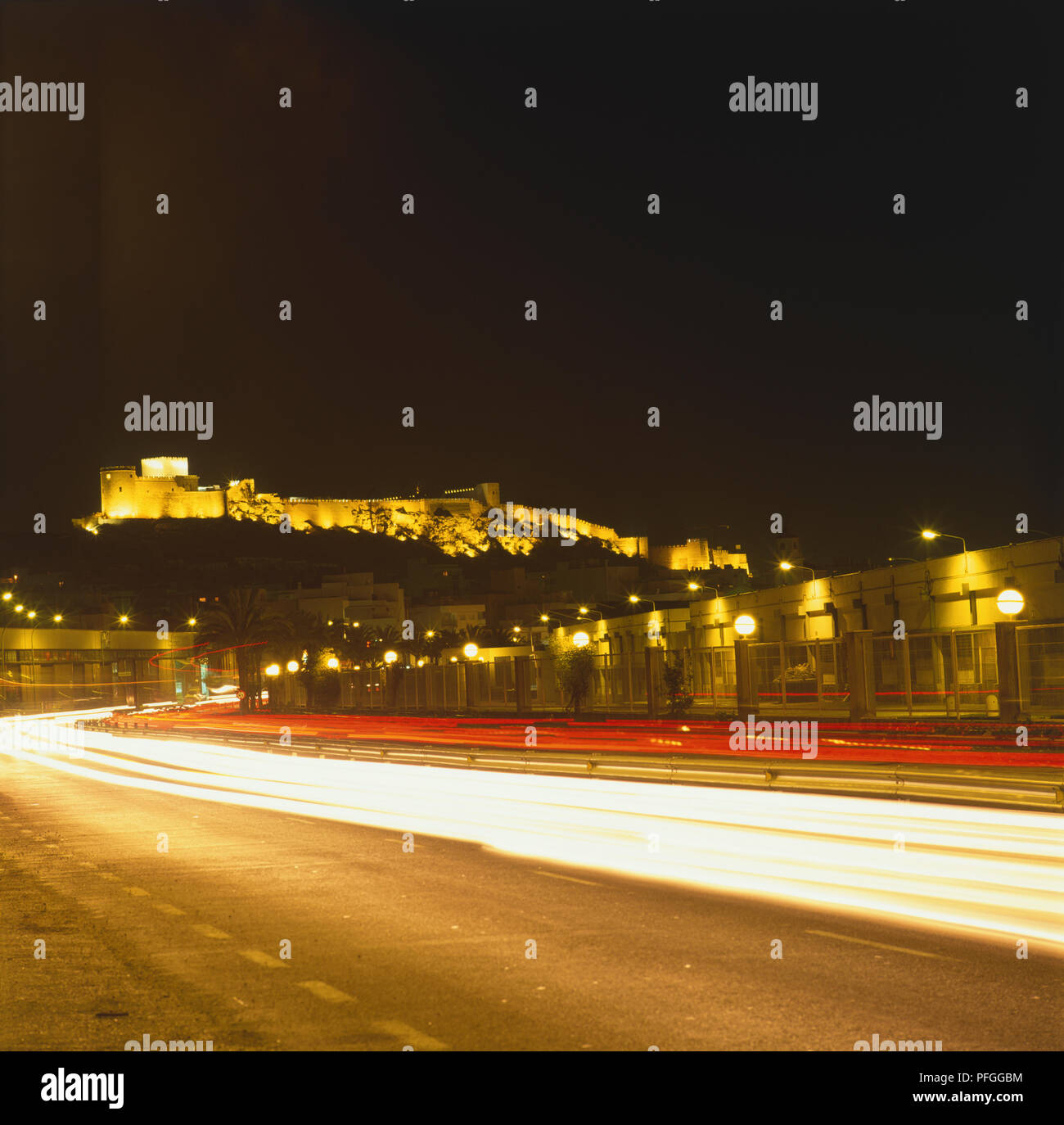 Spagna, Andalusia, Almeria, lunga esposizione della fortezza moresca di notte, streak delle luci auto in primo piano. Foto Stock