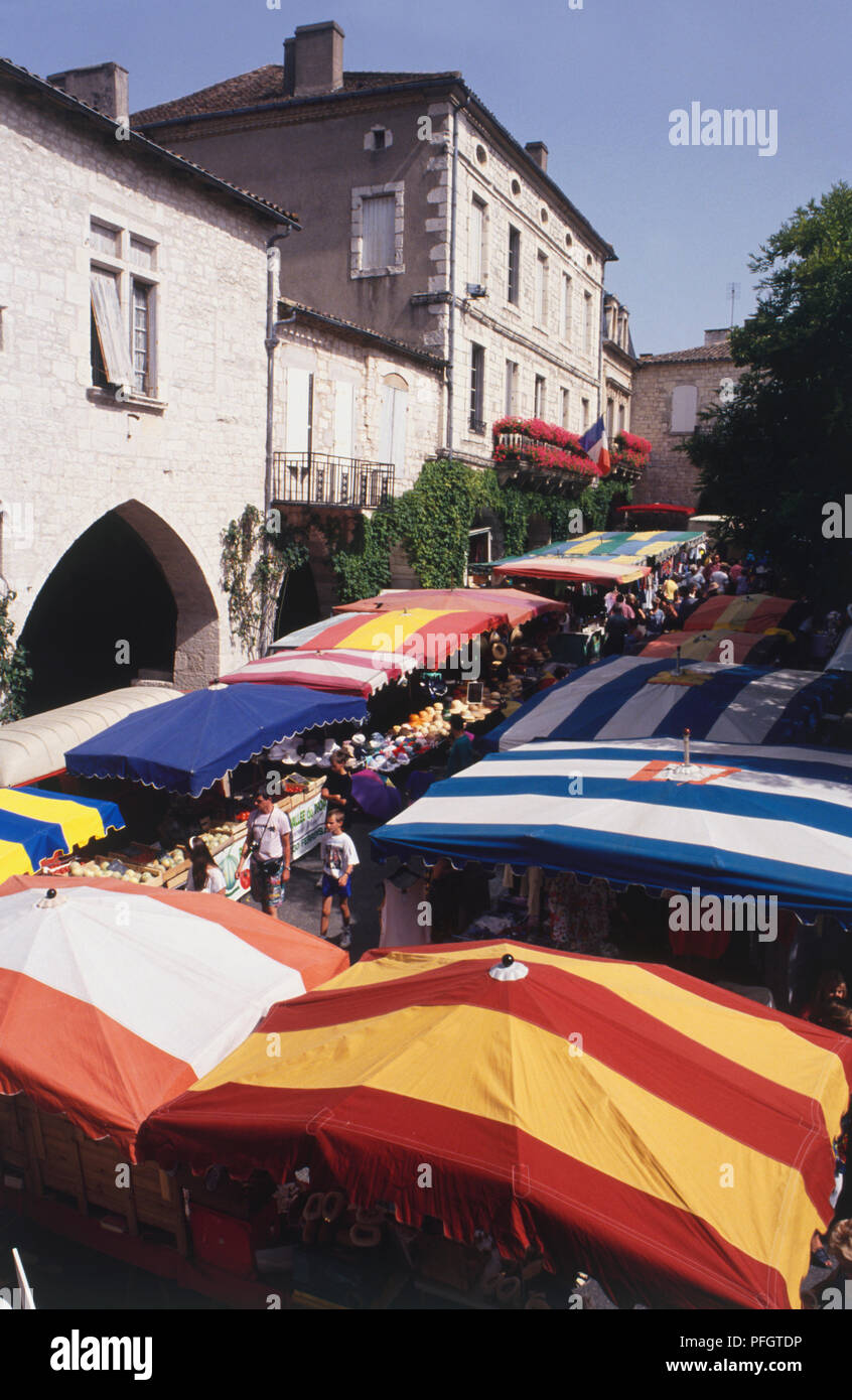 Francia, Montflanquin, strada costeggiata dai colori vivaci con il baldacchino bancarelle del mercato, vista in elevazione. Foto Stock