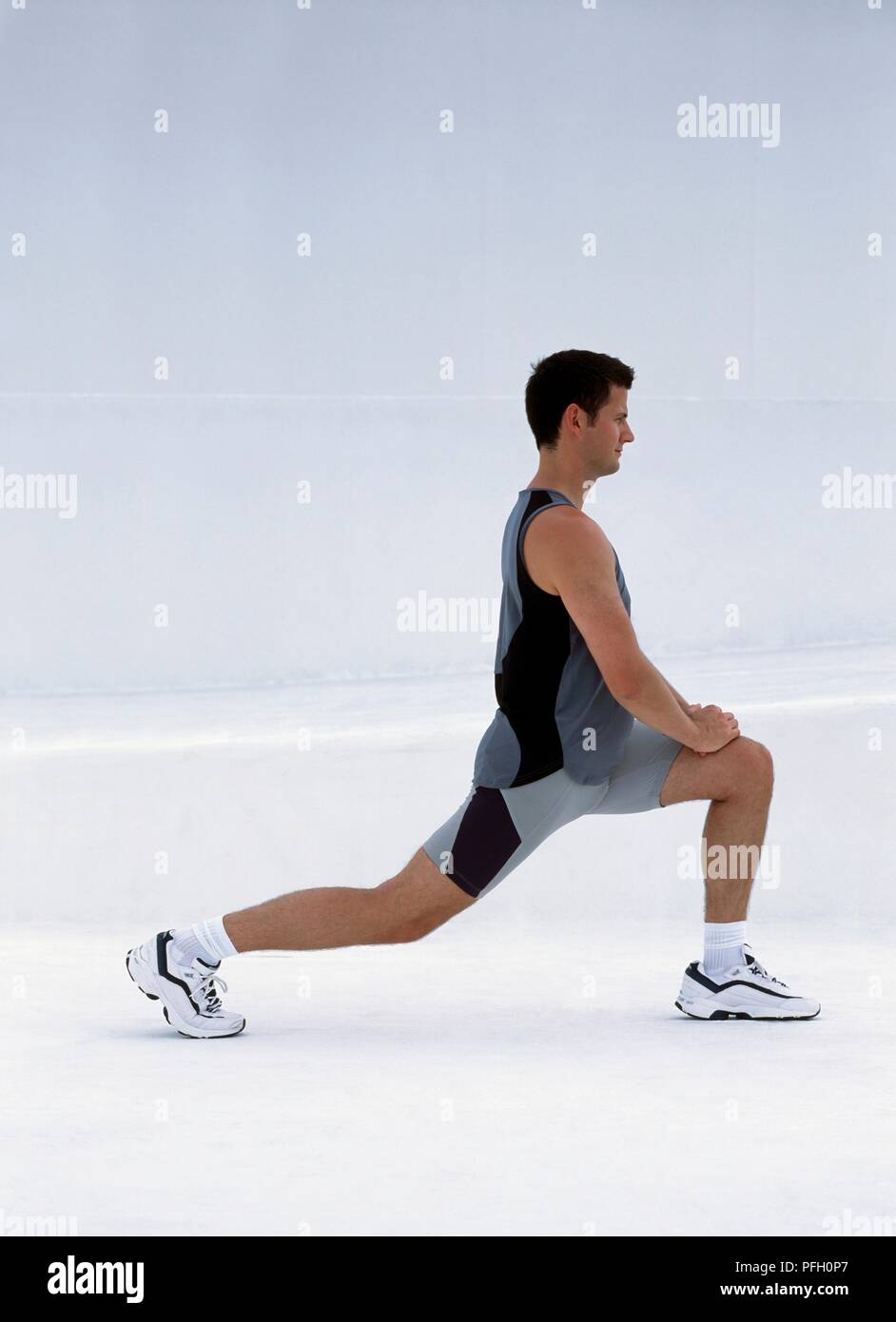 Uomo in pantaloncini corti e canotta eseguire esercizi di allungamento, vista laterale Foto Stock