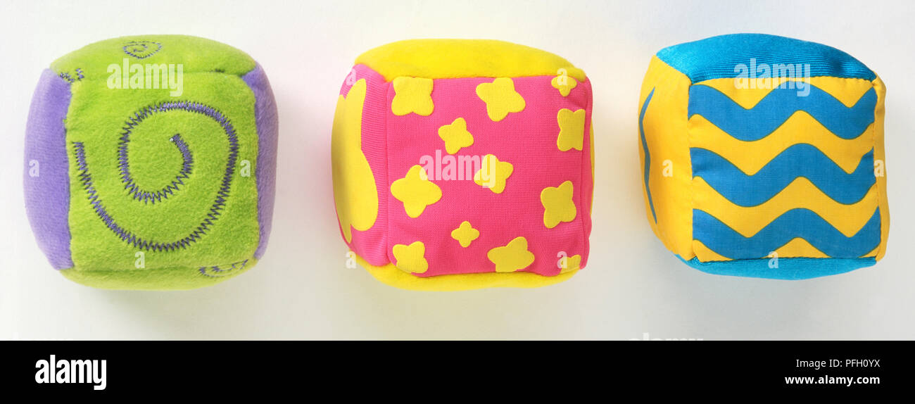 Quattro giocattolo morbido a cubetti, uno con squiggles blu su giallo, uno con fiori di colore giallo sul rosa, uno con viola volute su sfondo verde. Foto Stock