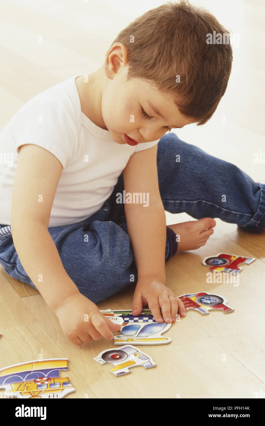I capelli castani boy bambino seduto sul pavimento a giocare con un puzzle Foto Stock